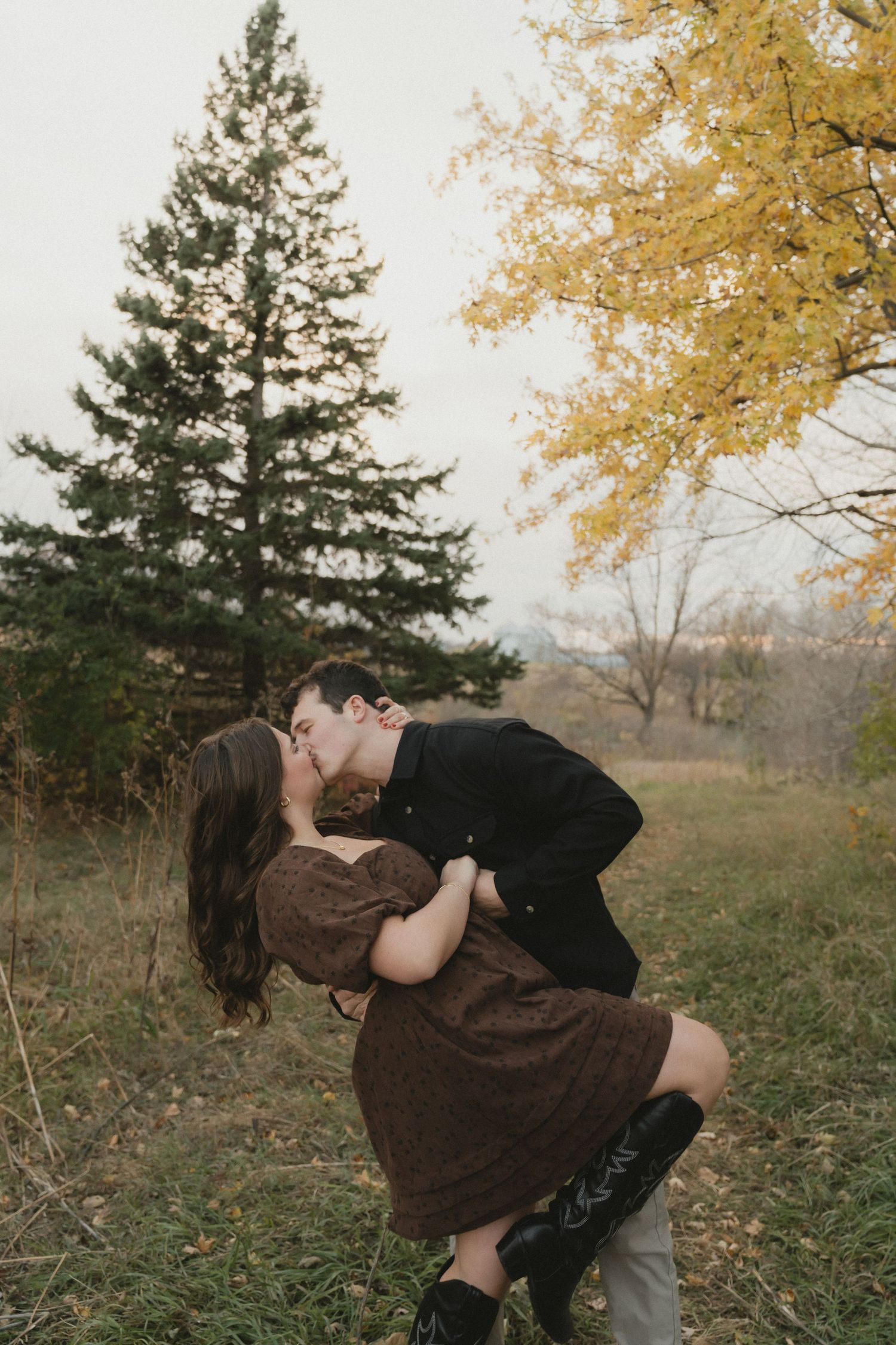 A romantic autumn scene with a couple embracing near evergreen and golden trees.