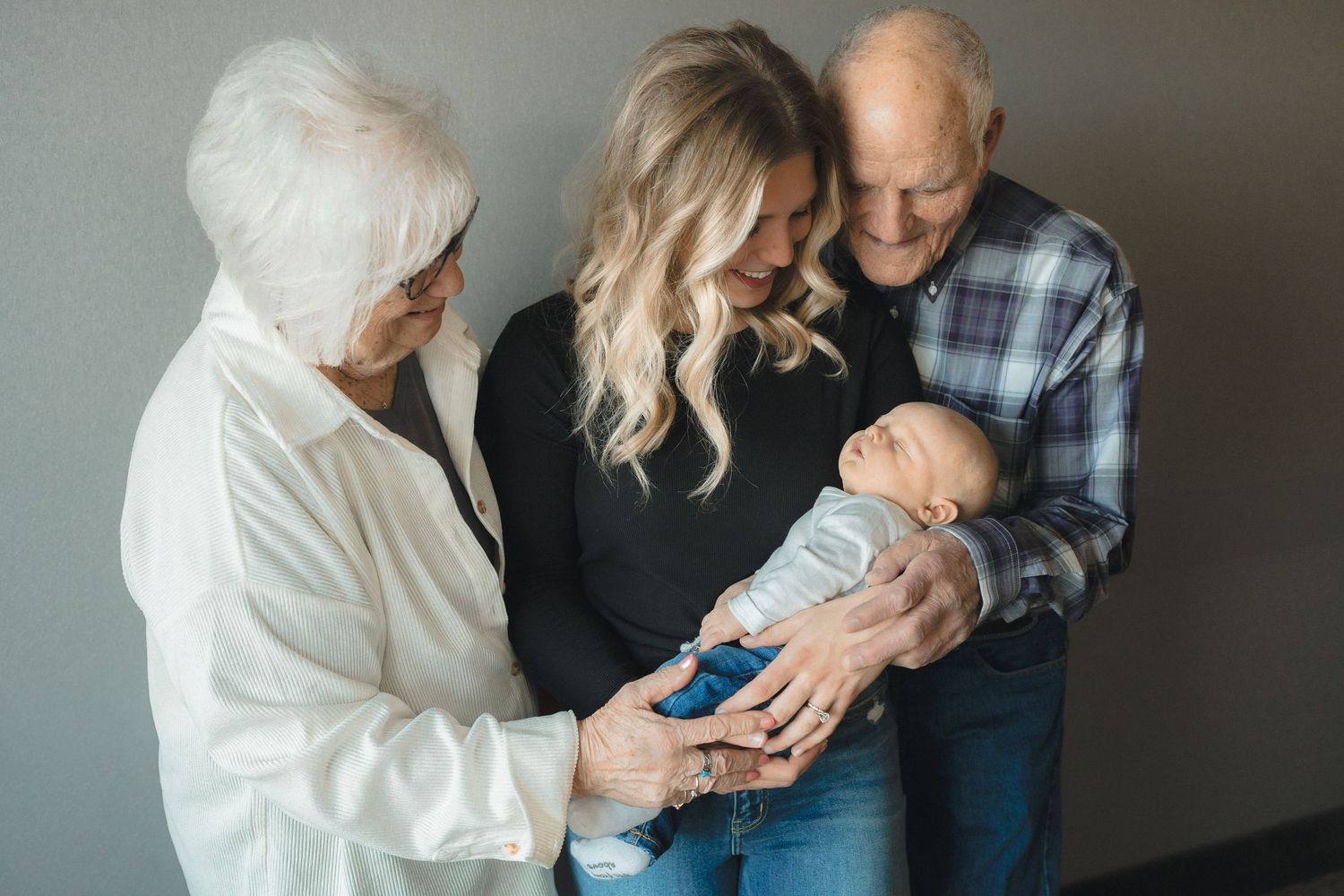 Grandparents and mother lovingly hold a newborn baby during a family portrait session indoors.