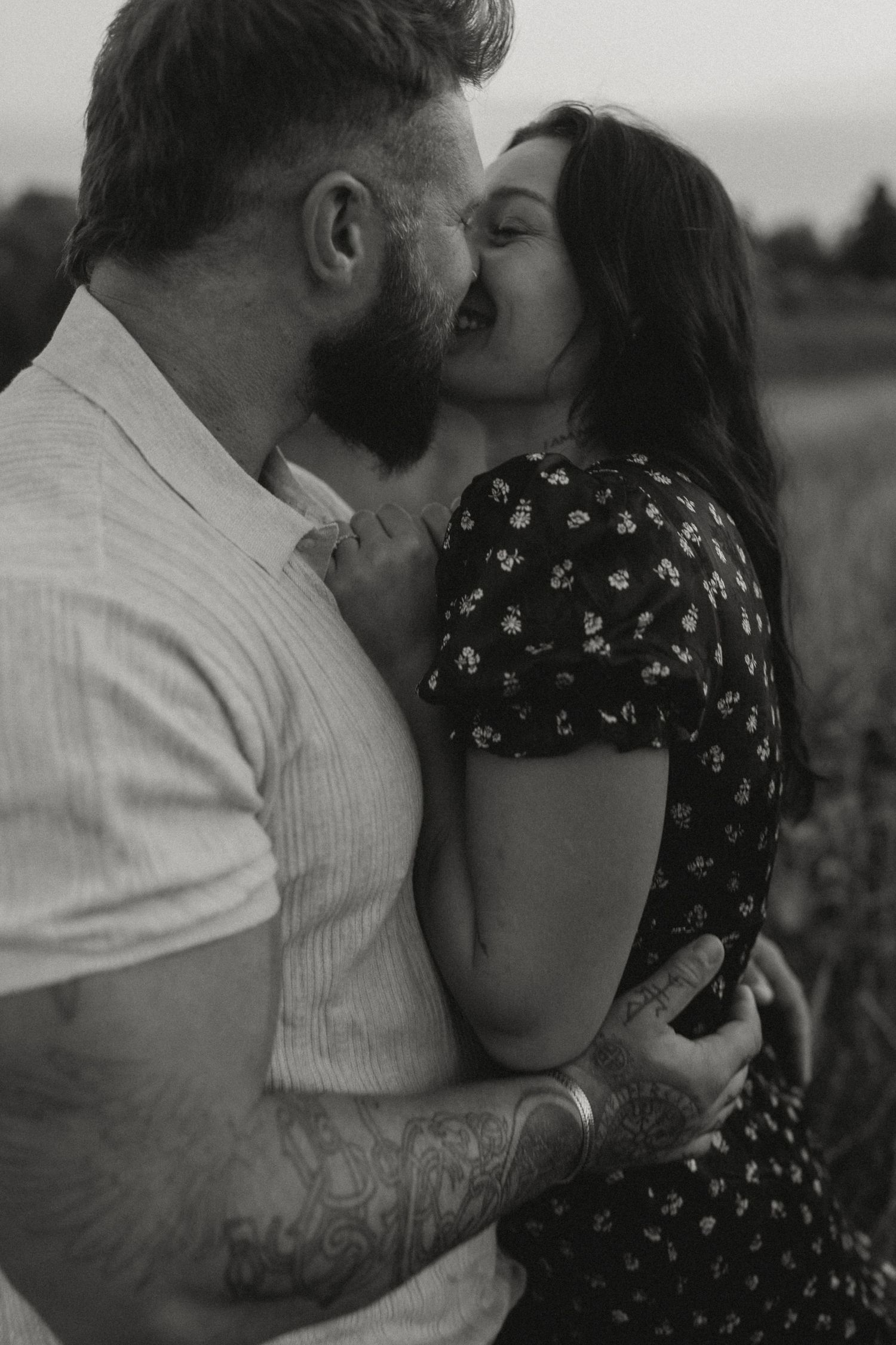 An intimate black and white portrait of a couple sharing a tender moment outdoors.