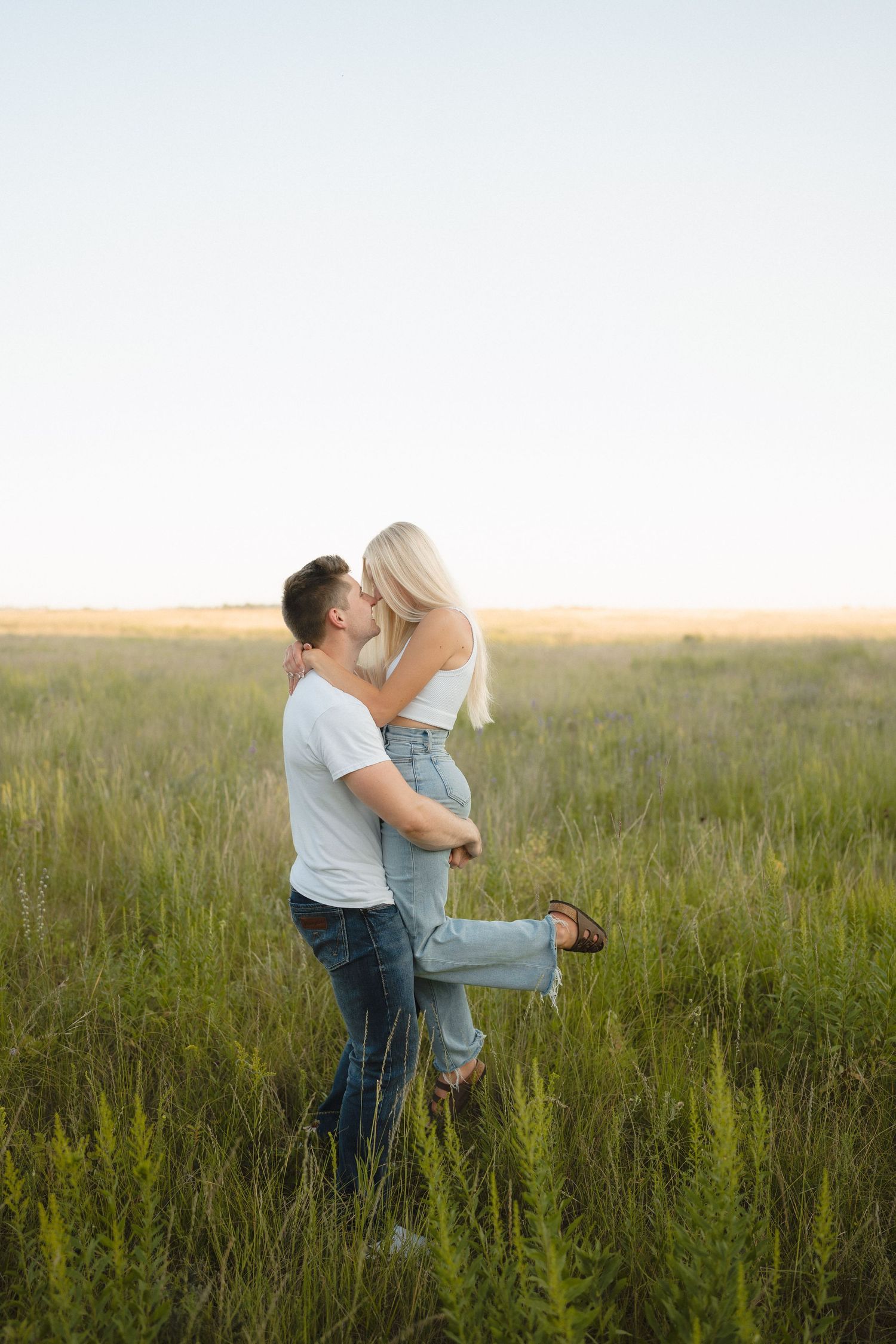 A romantic couple embraces in a golden field at sunset creating a dreamy silhouette against the horizon.