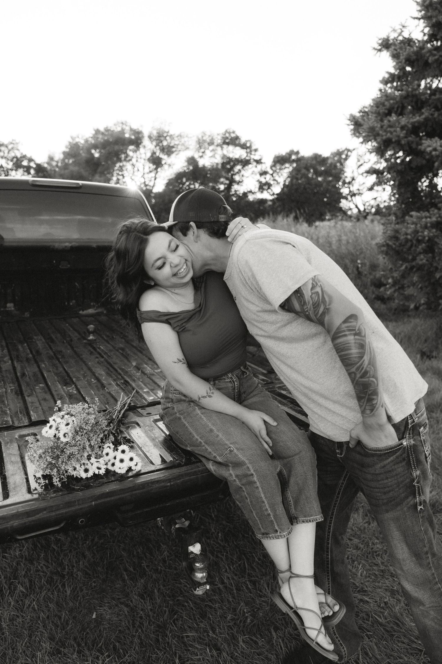A romantic black and white photo of a couple by a pickup truck bed with flowers.