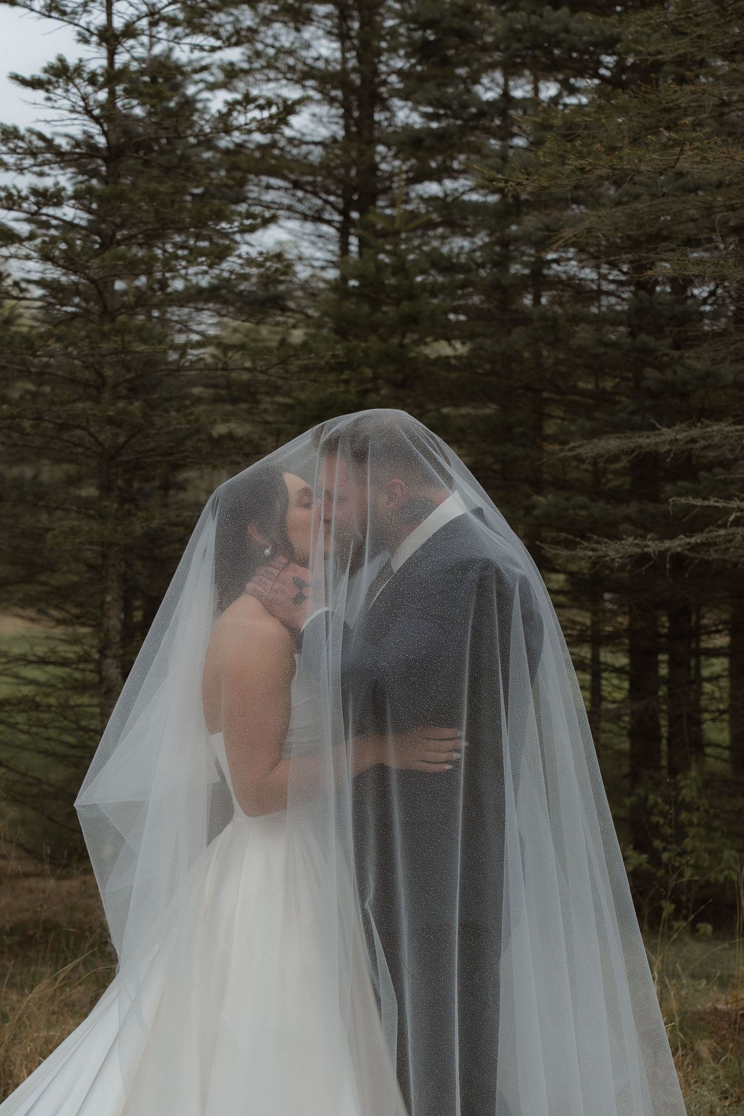 A romantic veil shot with evergreen trees creating a stunning natural backdrop.