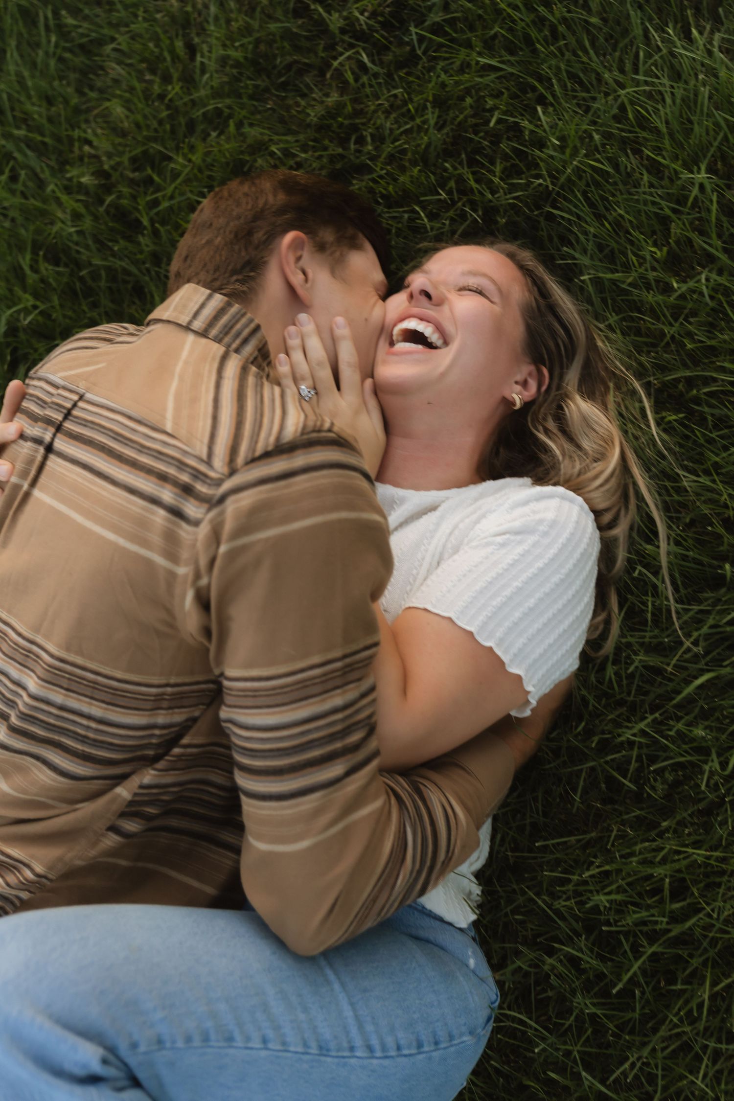 A couple shares a joyful moment while lying in green grass.