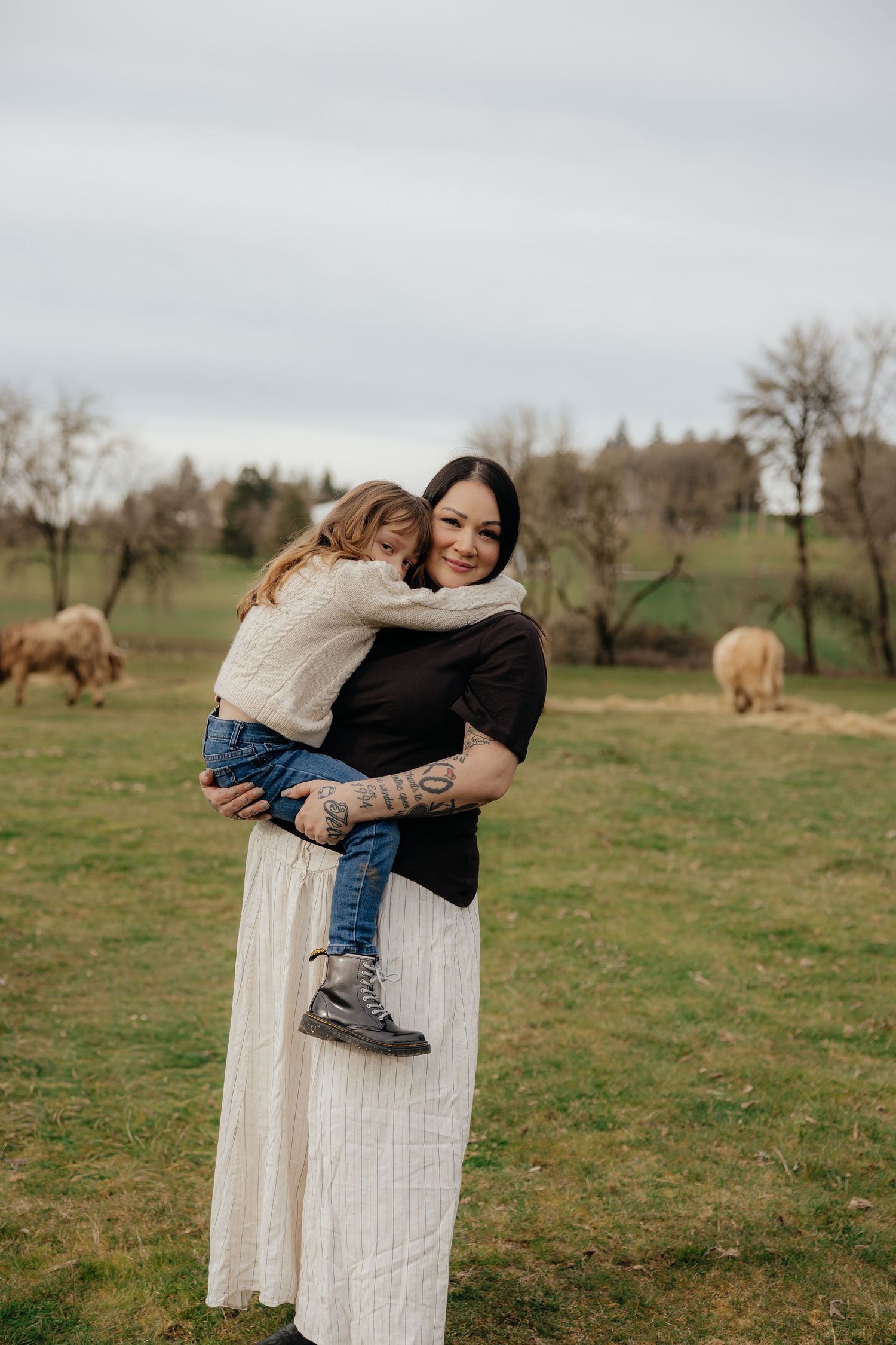A tender moment shared between parent and child in a pastoral field with hay bales and trees in the background.