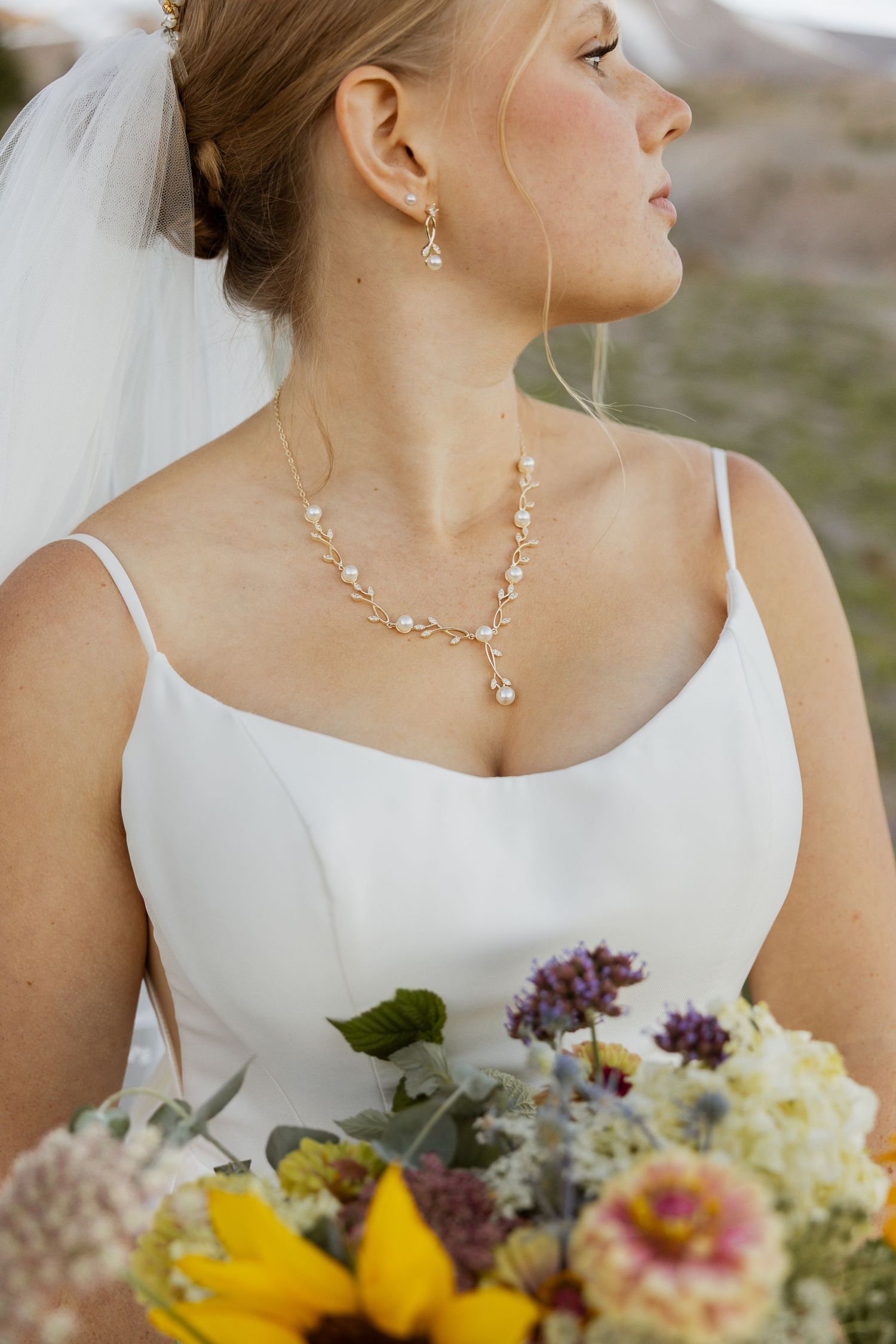 Elegant bridal portrait featuring delicate gold jewelry and a colorful wildflower bouquet.