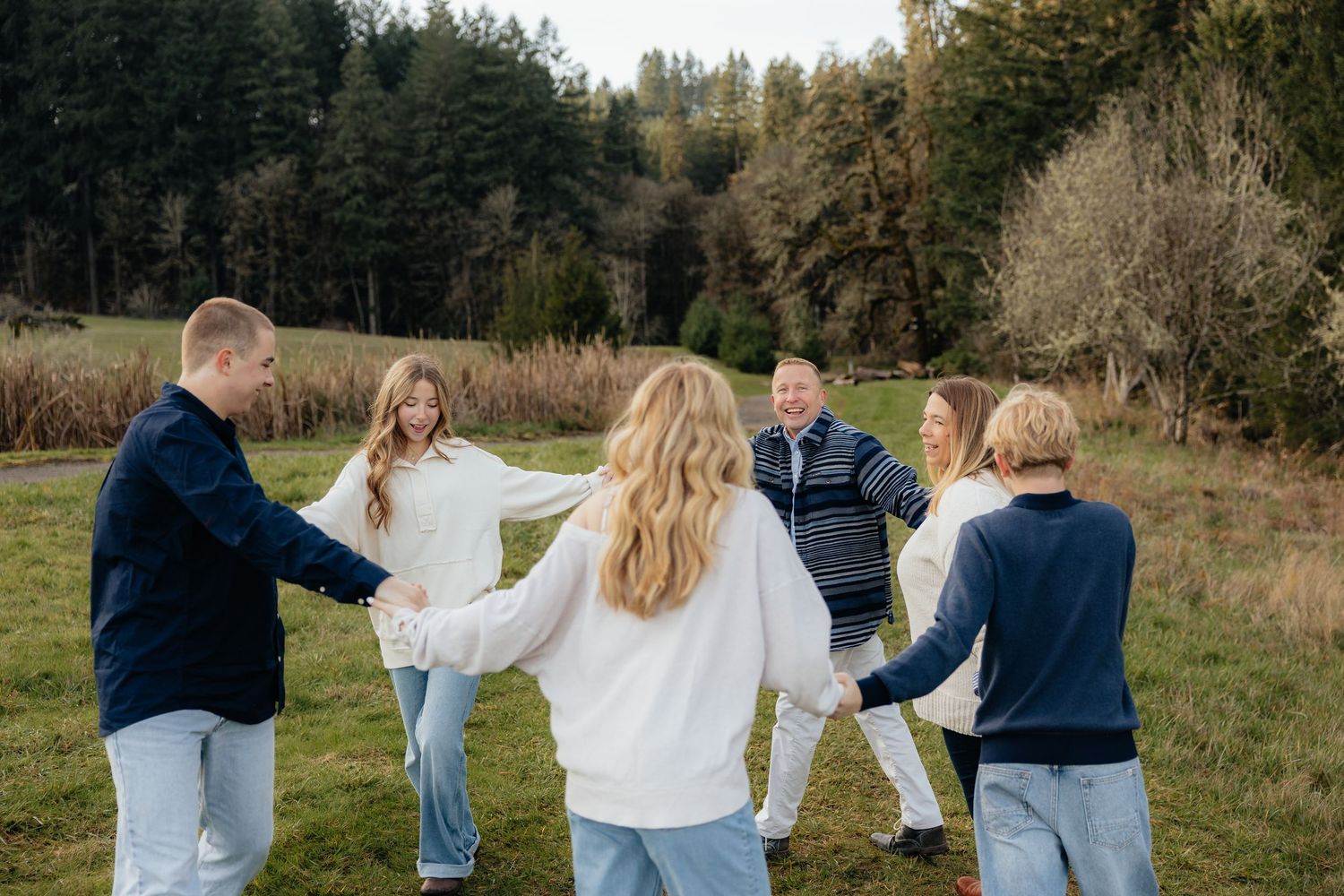 A family wearing navy and white outfits walks together through a grassy meadow at sunset.