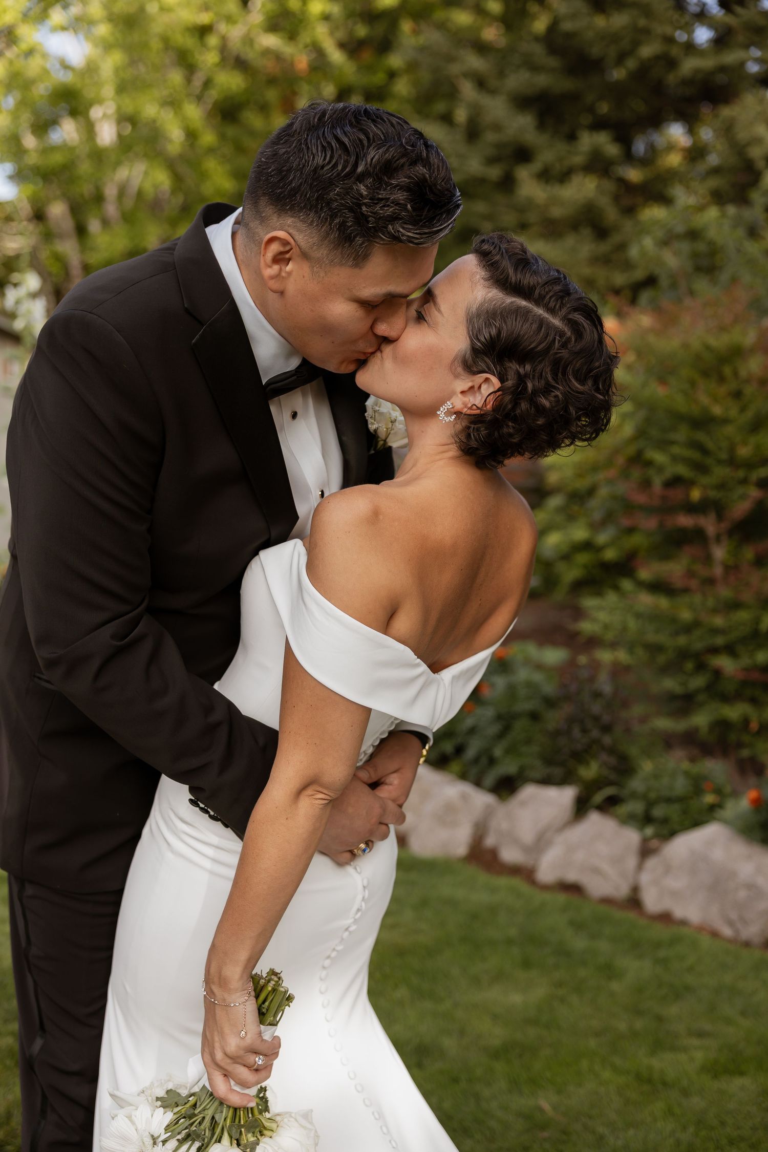 A romantic wedding couple sharing a dip kiss in an outdoor garden setting.