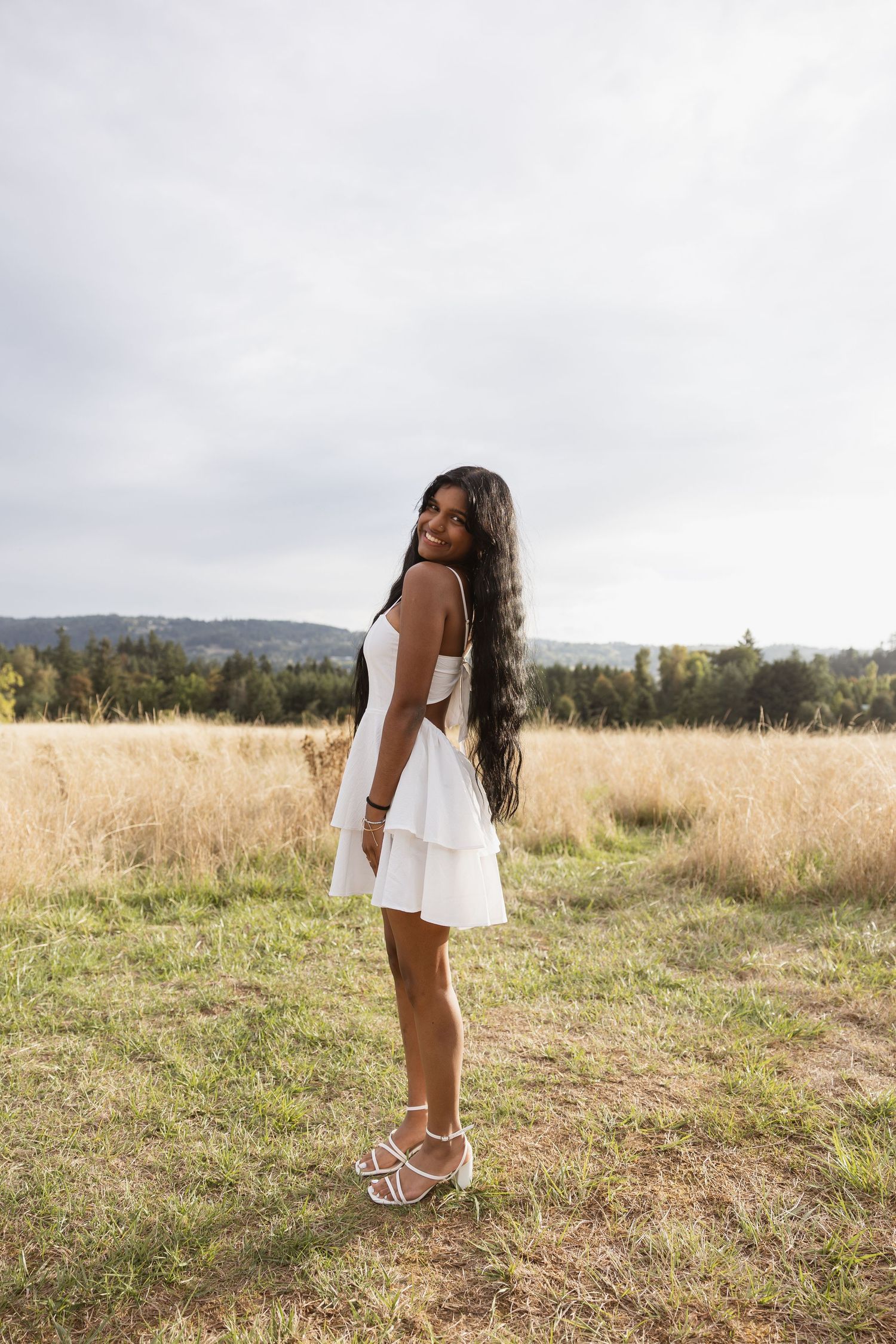 A person in a white dress stands thoughtfully in a golden meadow on a cloudy day.