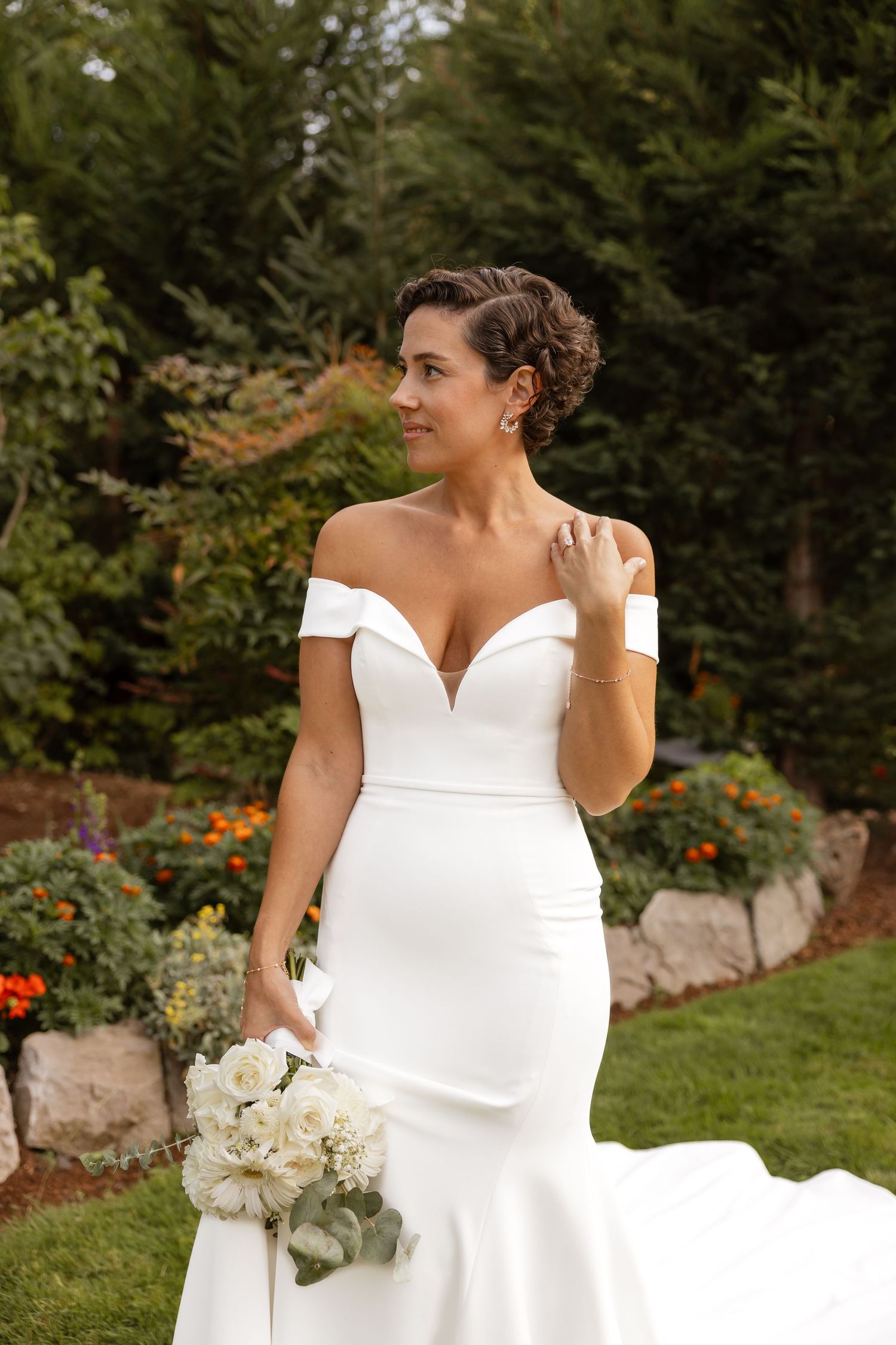 Elegant bride in fitted white wedding dress posing in garden setting.
