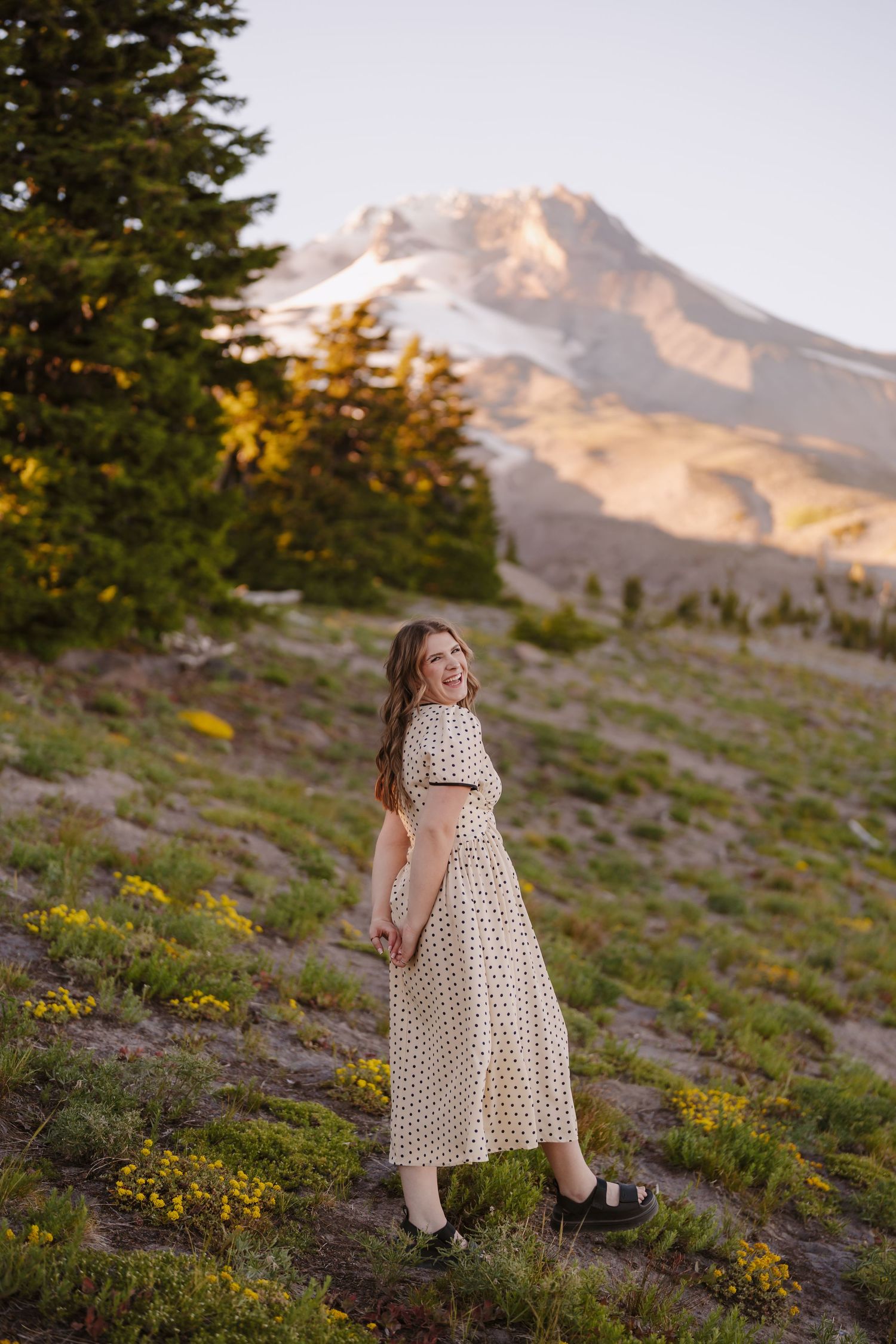 Young woman in polka dot dress smiling at Mount Hood meadow during golden hour sunset in Oregon.