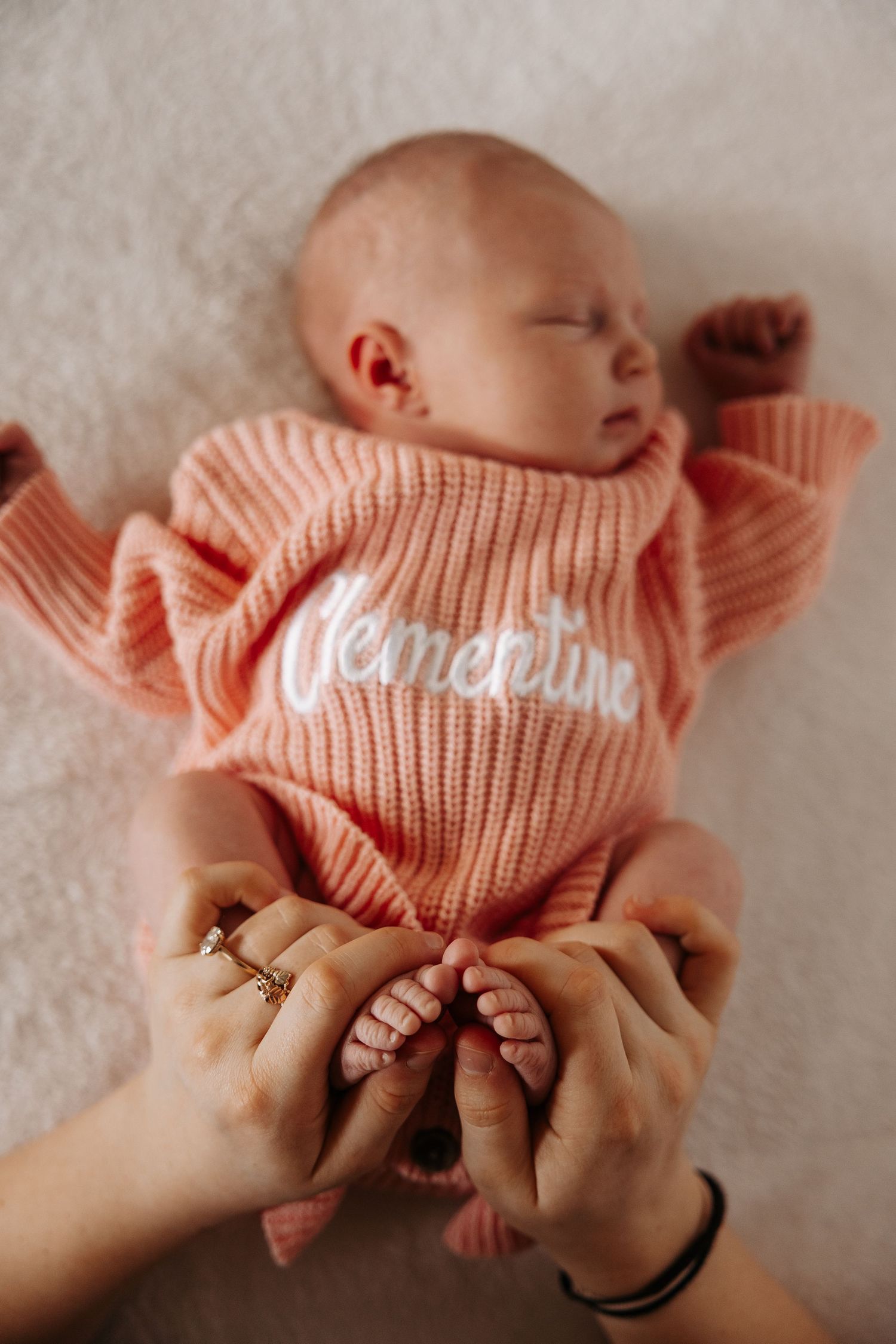 A series of hands holding and adjusting a peach-colored knit sweater on a tiny baby against a soft white background.