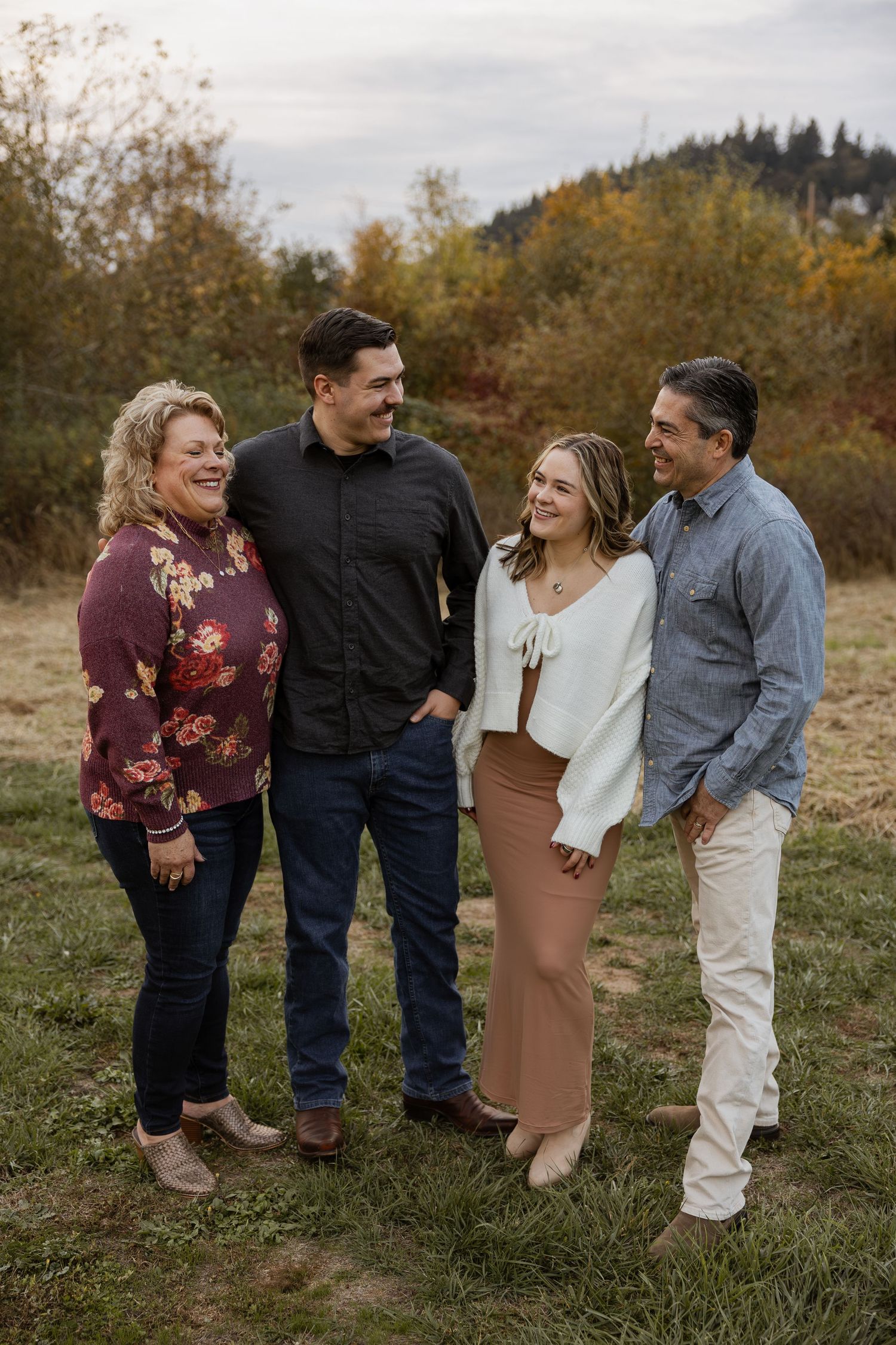 Group of four people laughing together in a field during autumn with trees in the background.