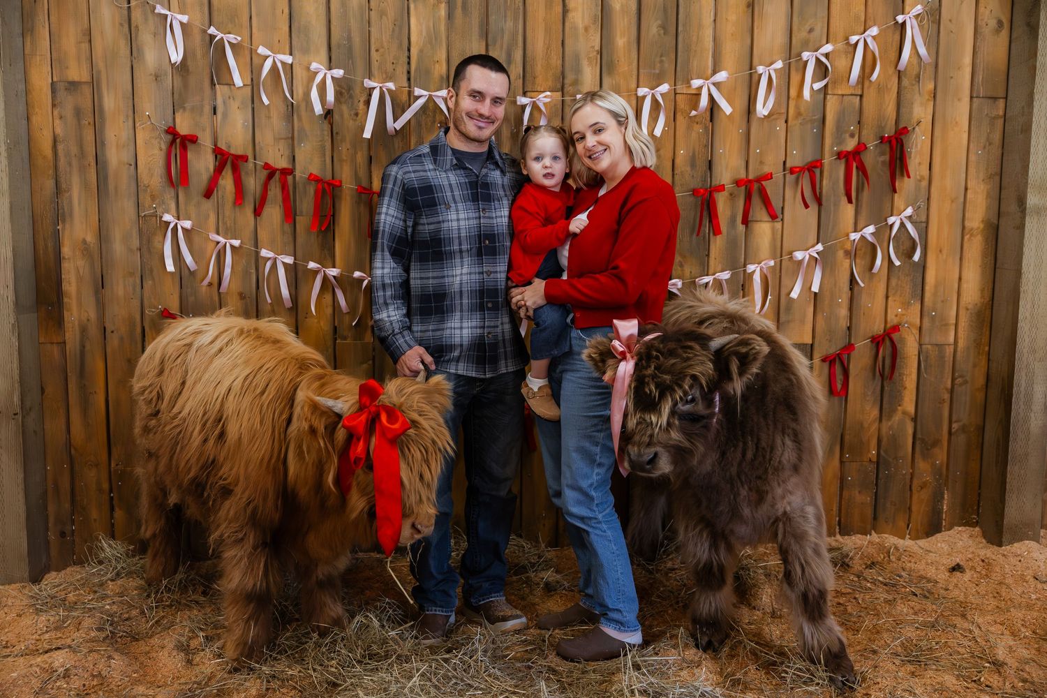 Family poses with their chocolate Labrador retriever in front of a rustic wooden fence with holiday decorations.