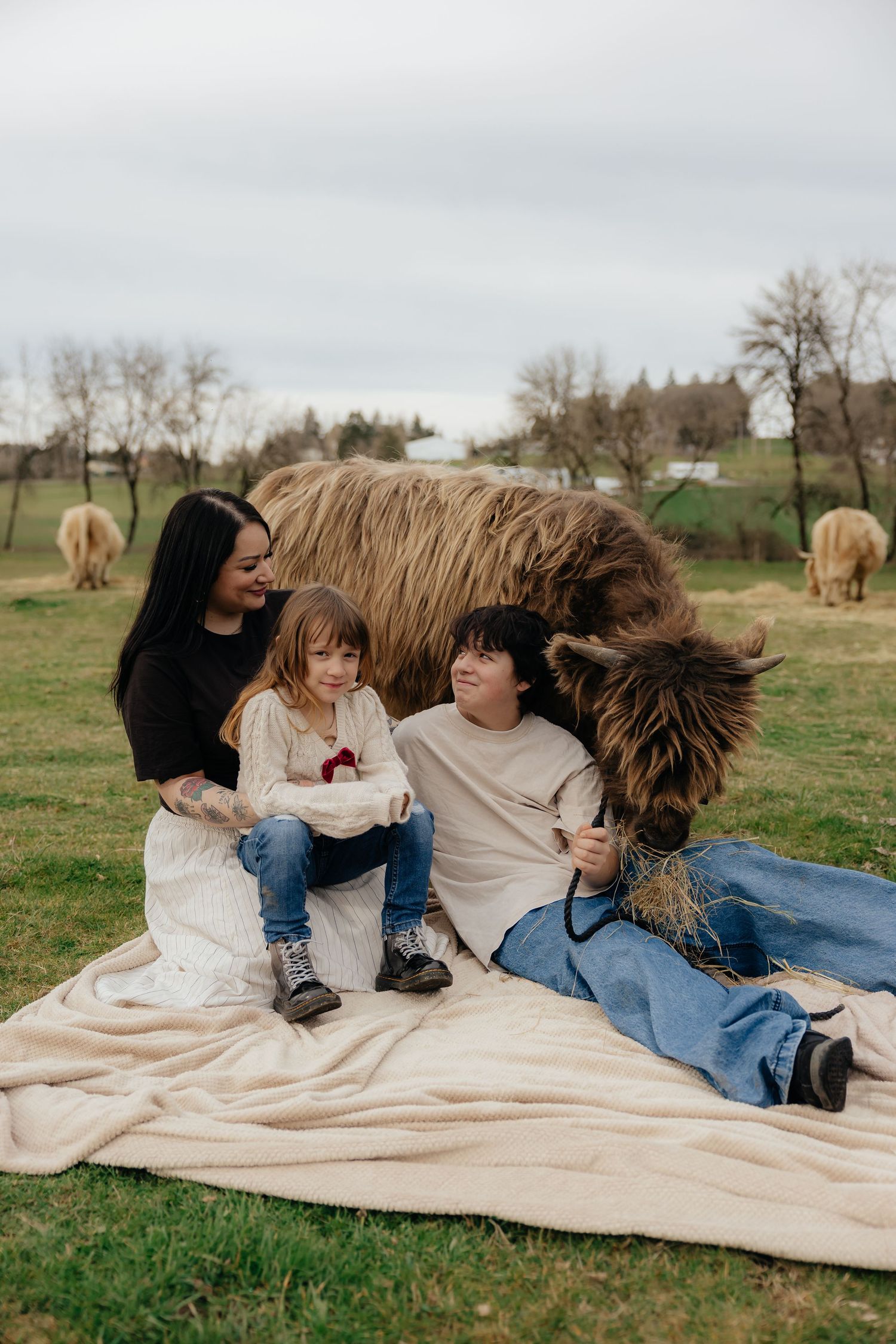 Family relaxing together on a blanket in a grassy field on an overcast day.