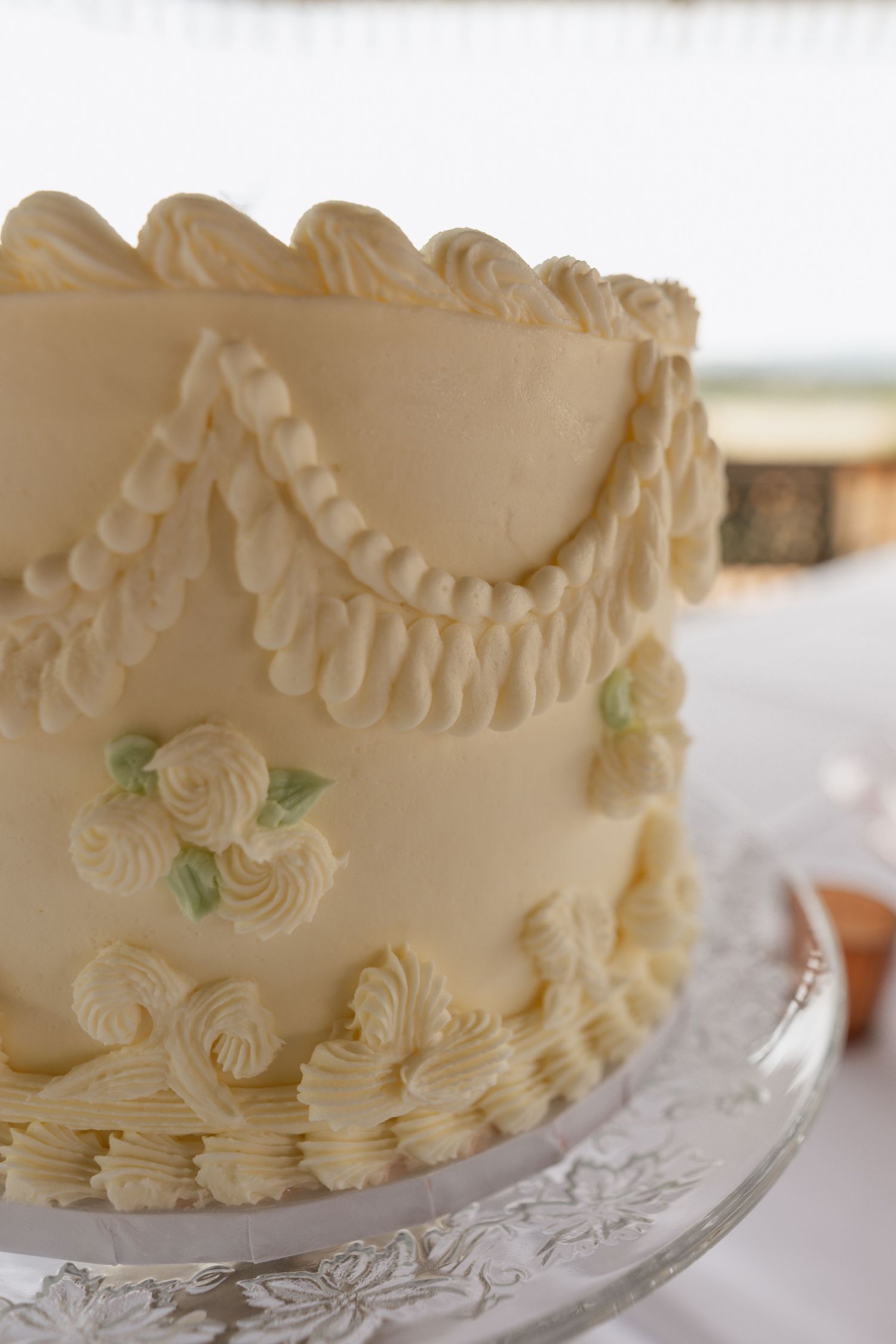 Elegant white wedding cake with intricate piped details and floral decorations on crystal plate.