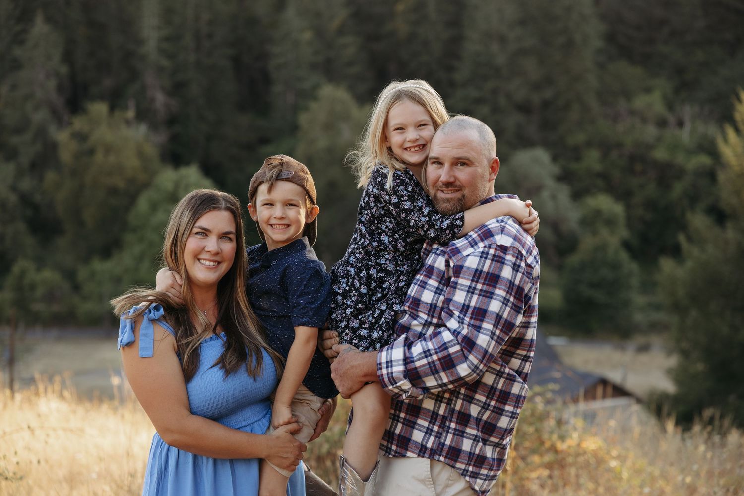 A family shares tender moments together in a natural outdoor setting with evergreen trees in the background.
