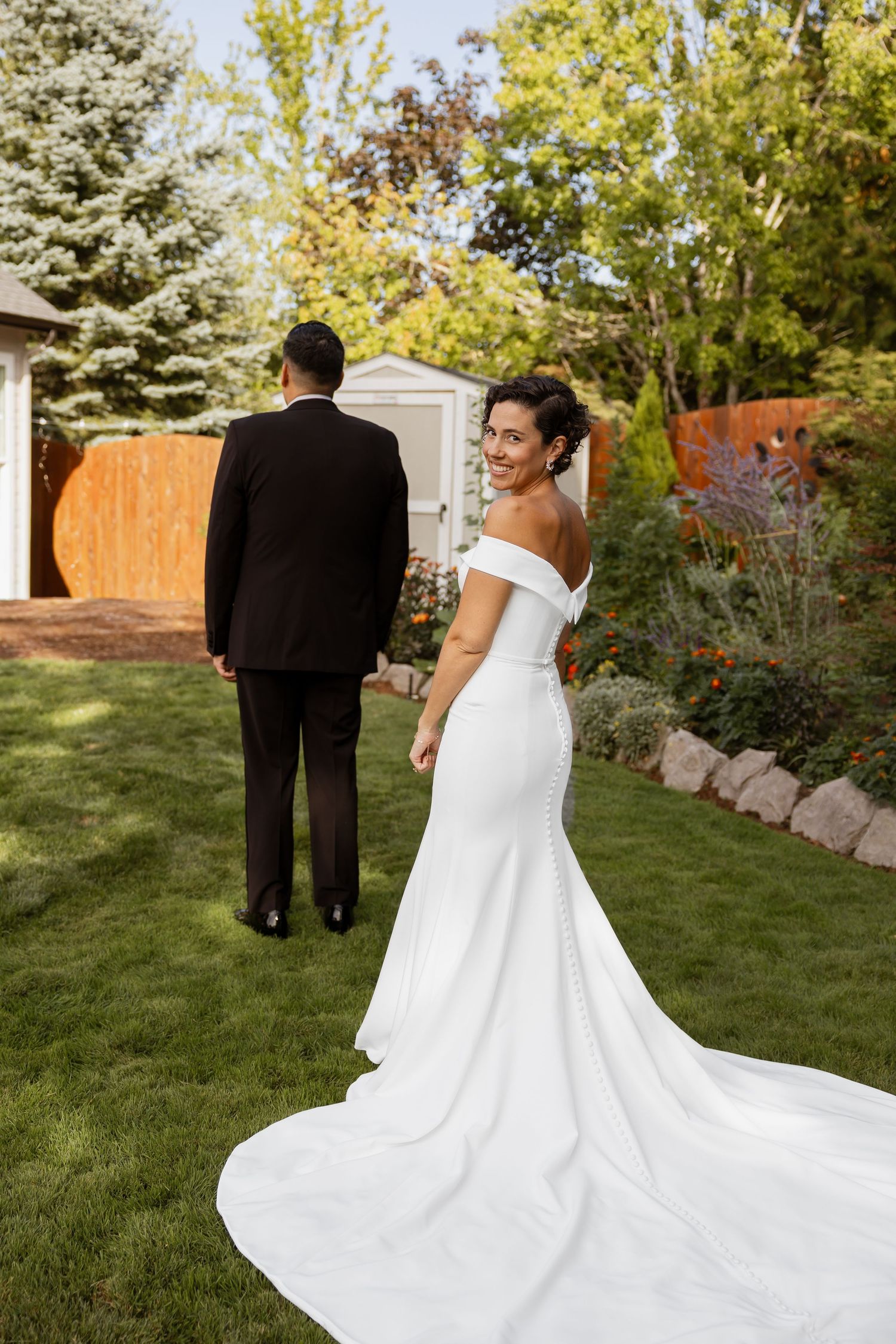 Elegant wedding couple poses in a garden setting with flowing white dress and classic black tuxedo.