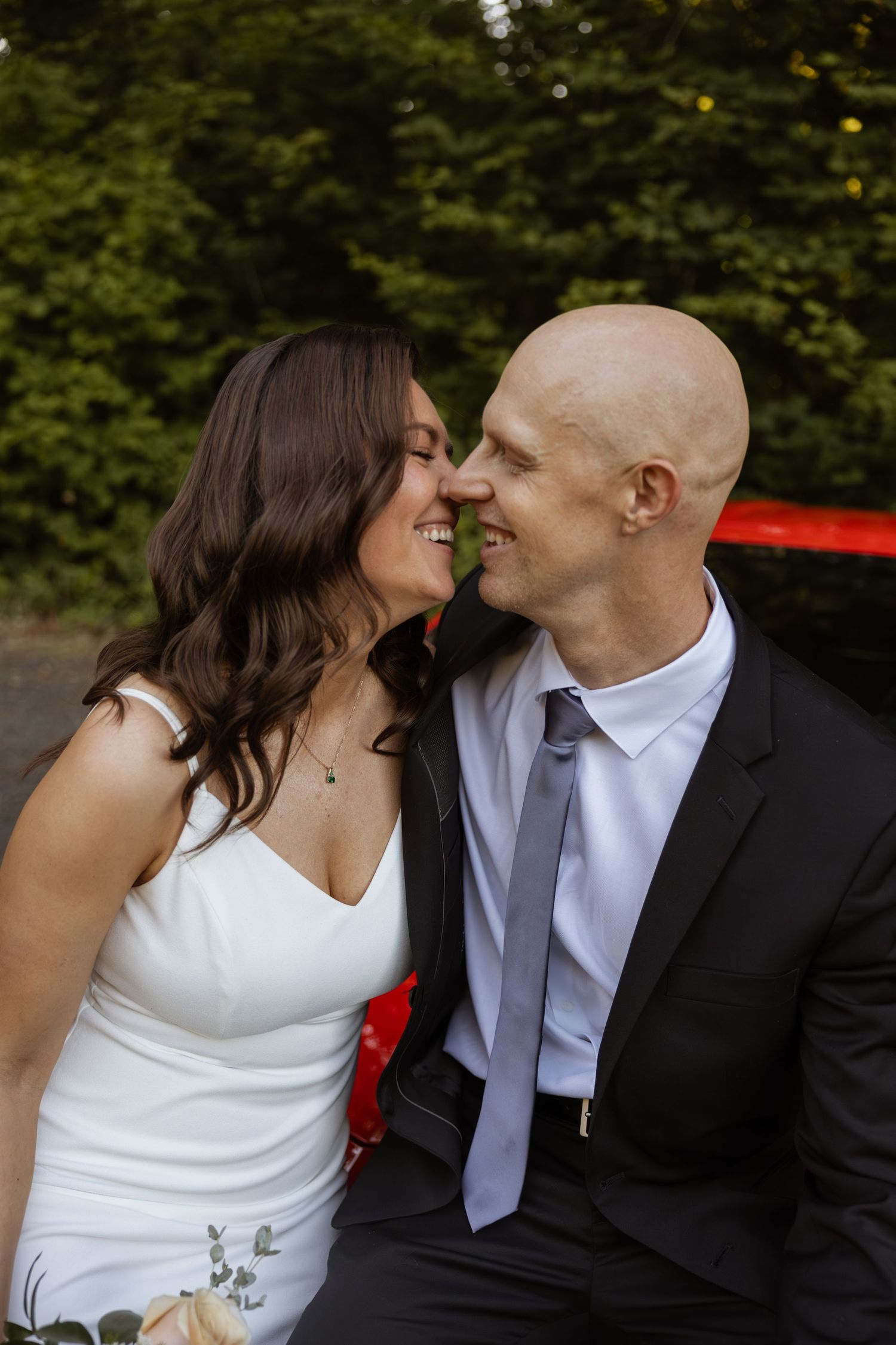 A couple in wedding attire share intimate moments and laughter while posing together outdoors.