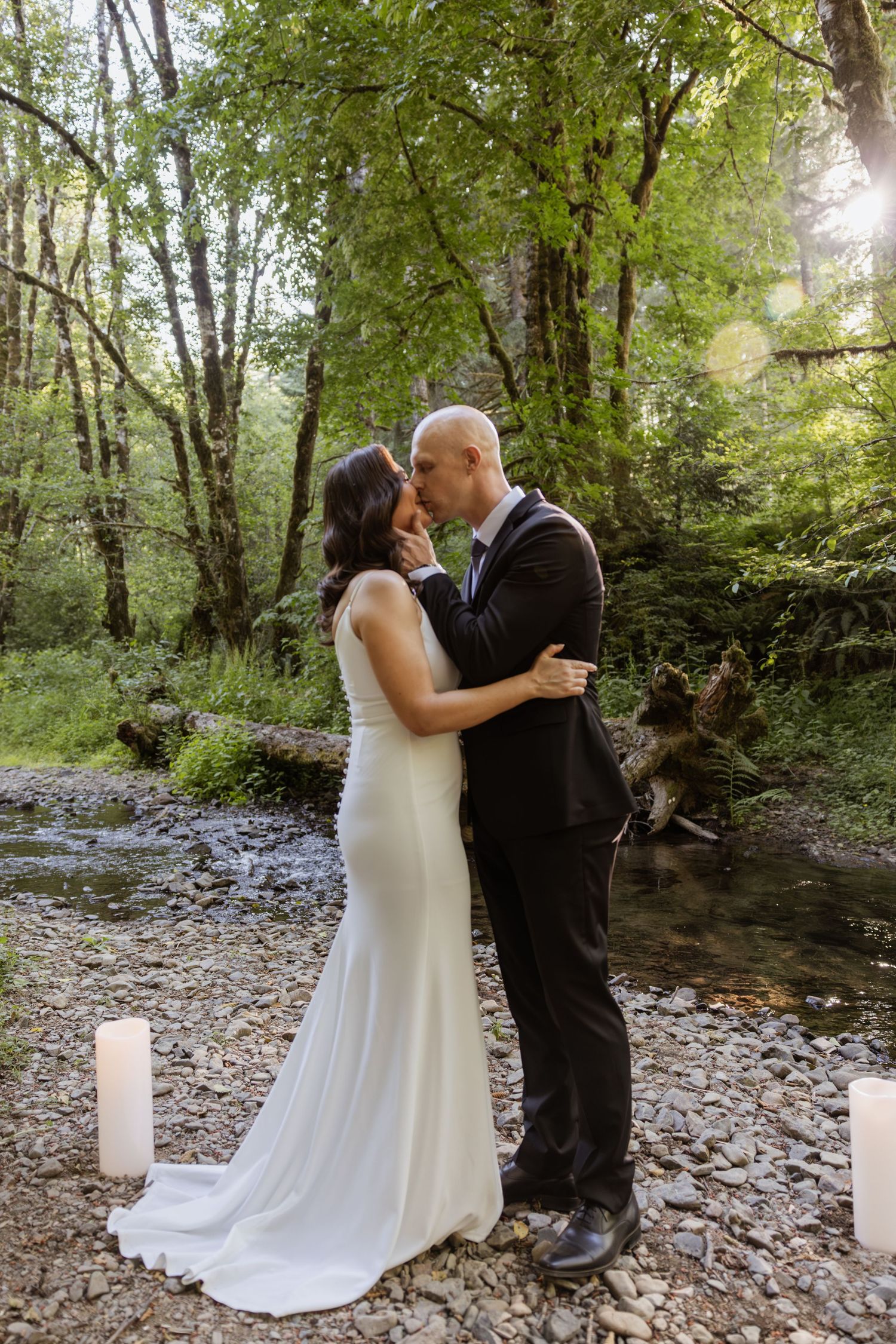 A romantic wedding couple shares an intimate dance in a serene forest setting with white candles lining the ground.