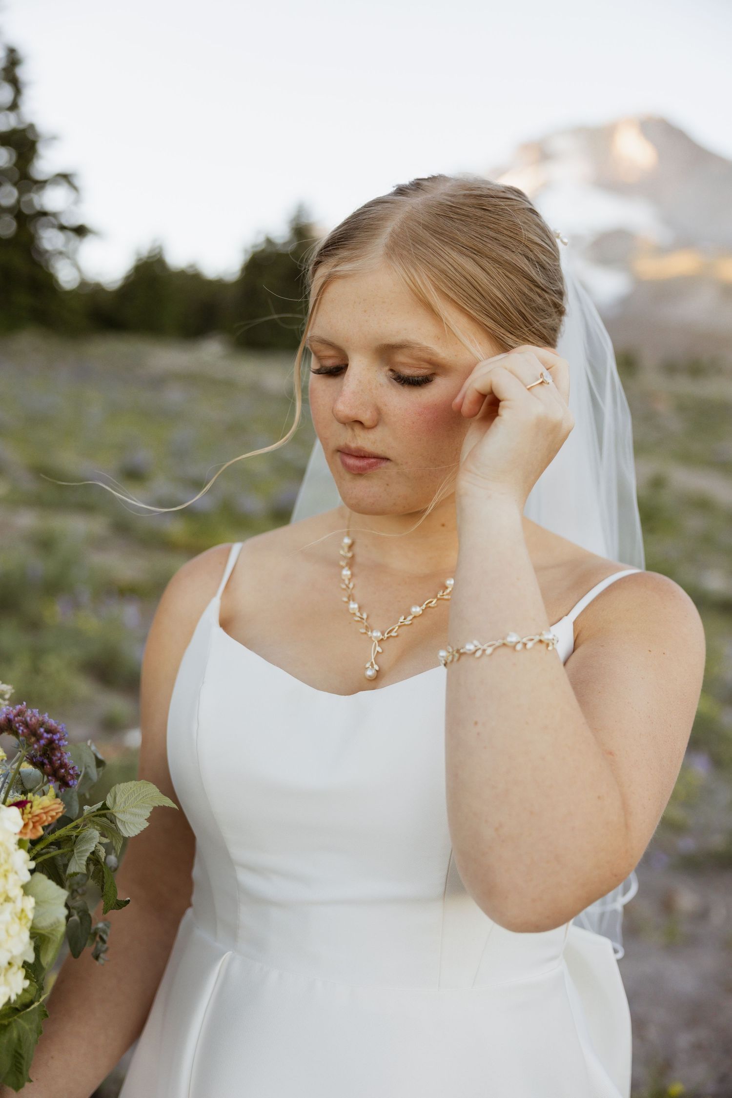Close-up portraits of a bride in a white dress wearing delicate jewelry against a mountain backdrop.
