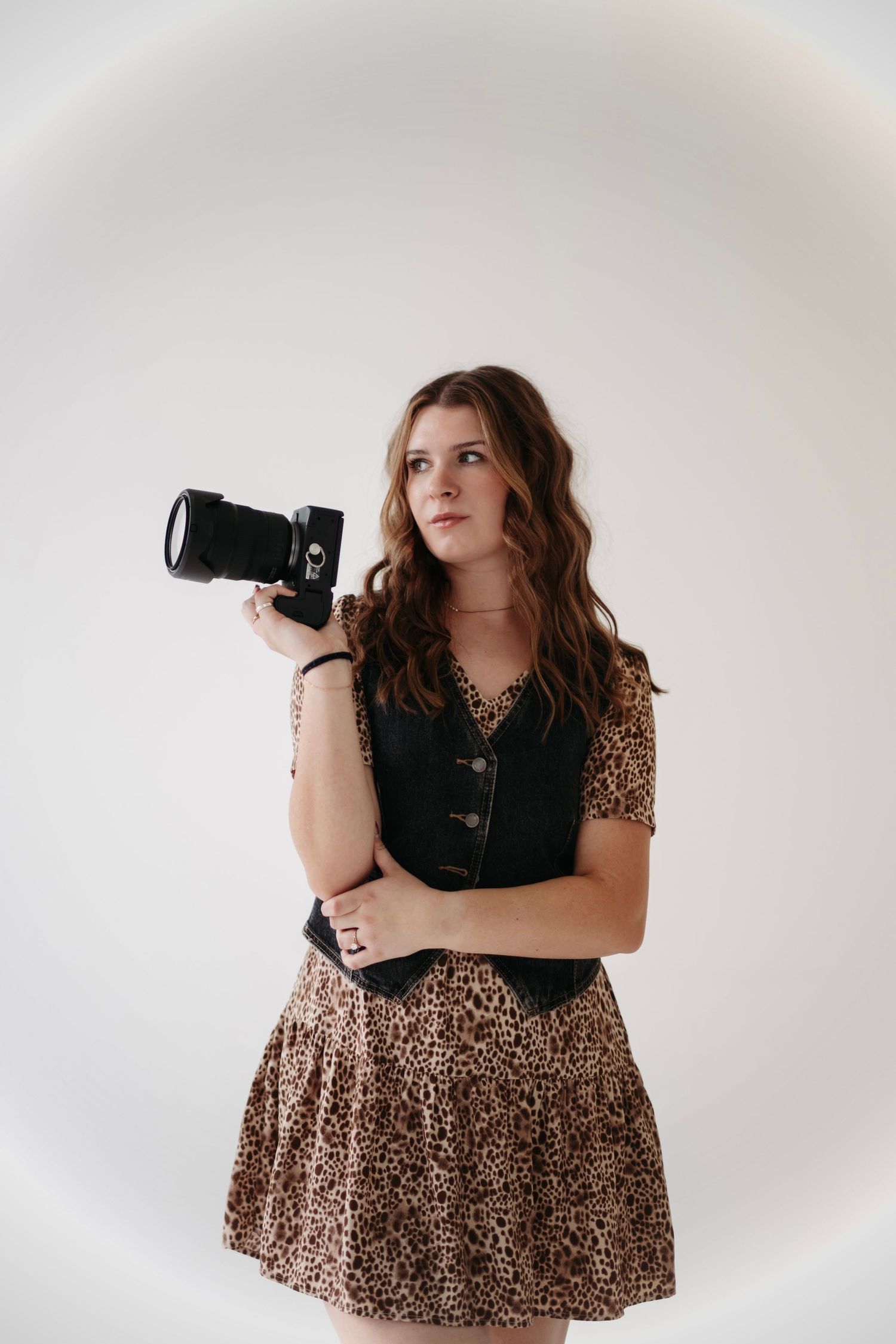 Professional photographer in leopard print dress posing with camera in studio.
