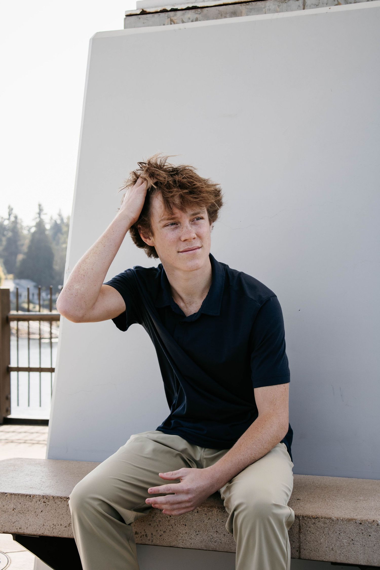 Young person in black t-shirt and khaki pants sitting casually on concrete ledge in outdoor setting.