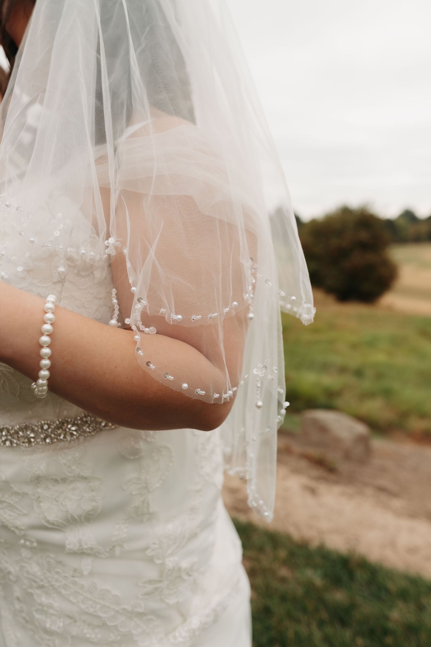Detail shot of delicate pearl-adorned wedding veil against natural outdoor background.