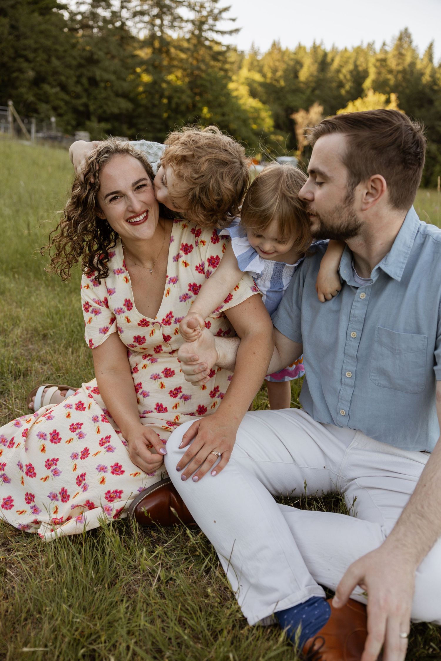 A family shares joyful moments together while relaxing on grass in a sun-dappled outdoor setting.
