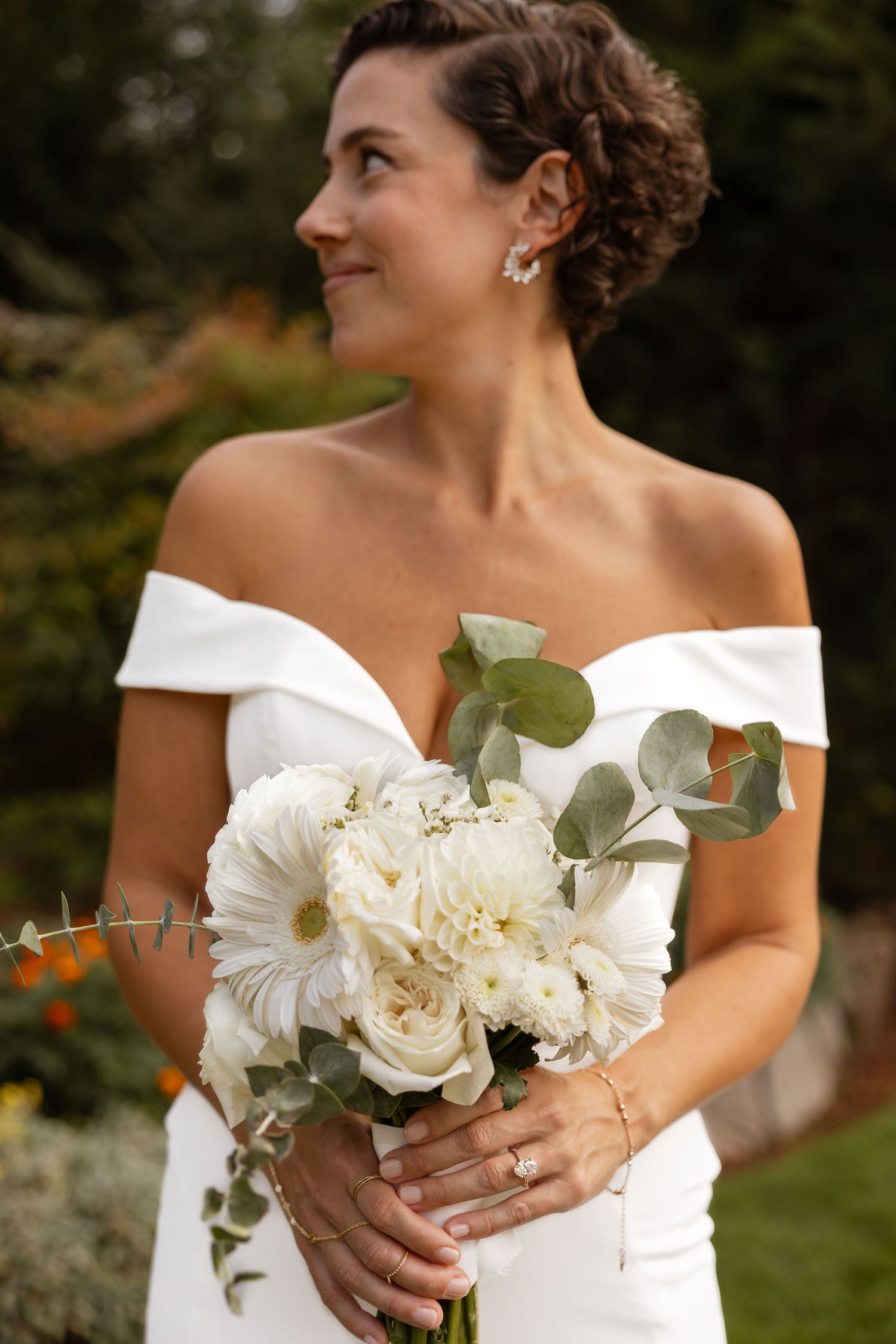 Bride holds a stunning white rose and eucalyptus bouquet against her off-shoulder wedding dress.