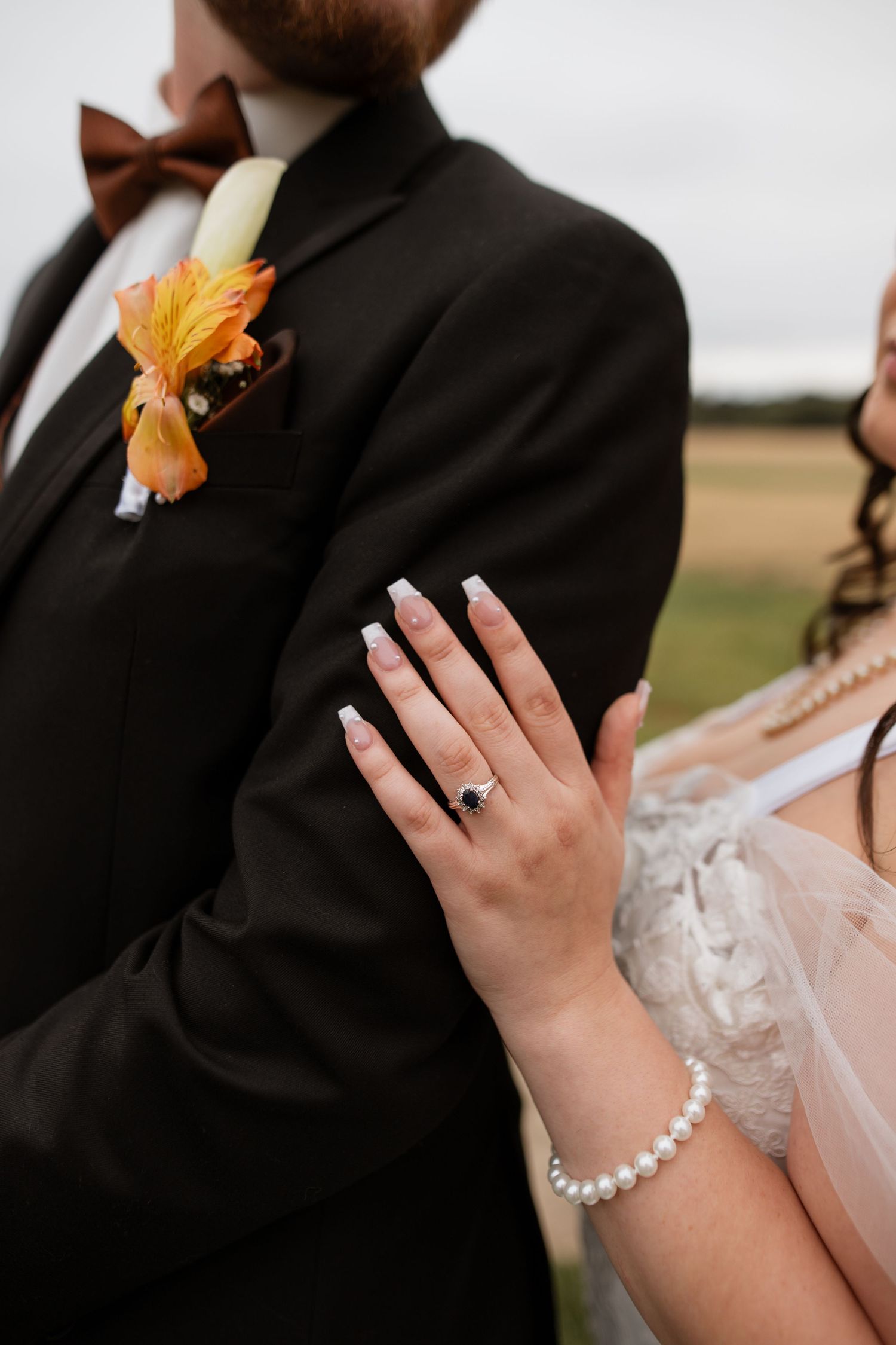 Close-up of wedding jewelry and orange boutonniere details against formal attire.