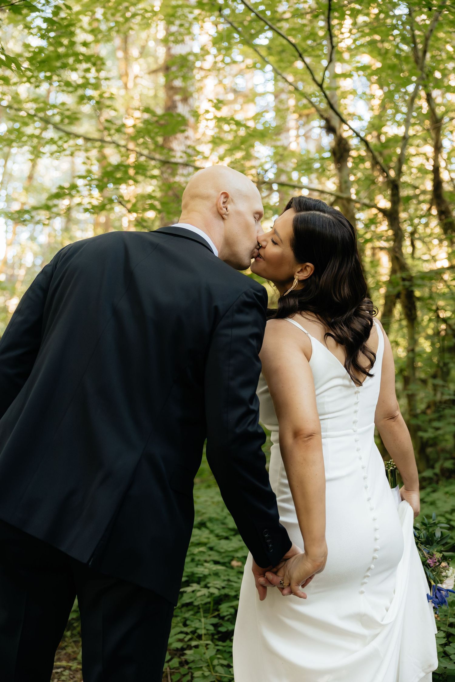 A romantic kiss in a lush forest setting with sunlight filtering through the trees.