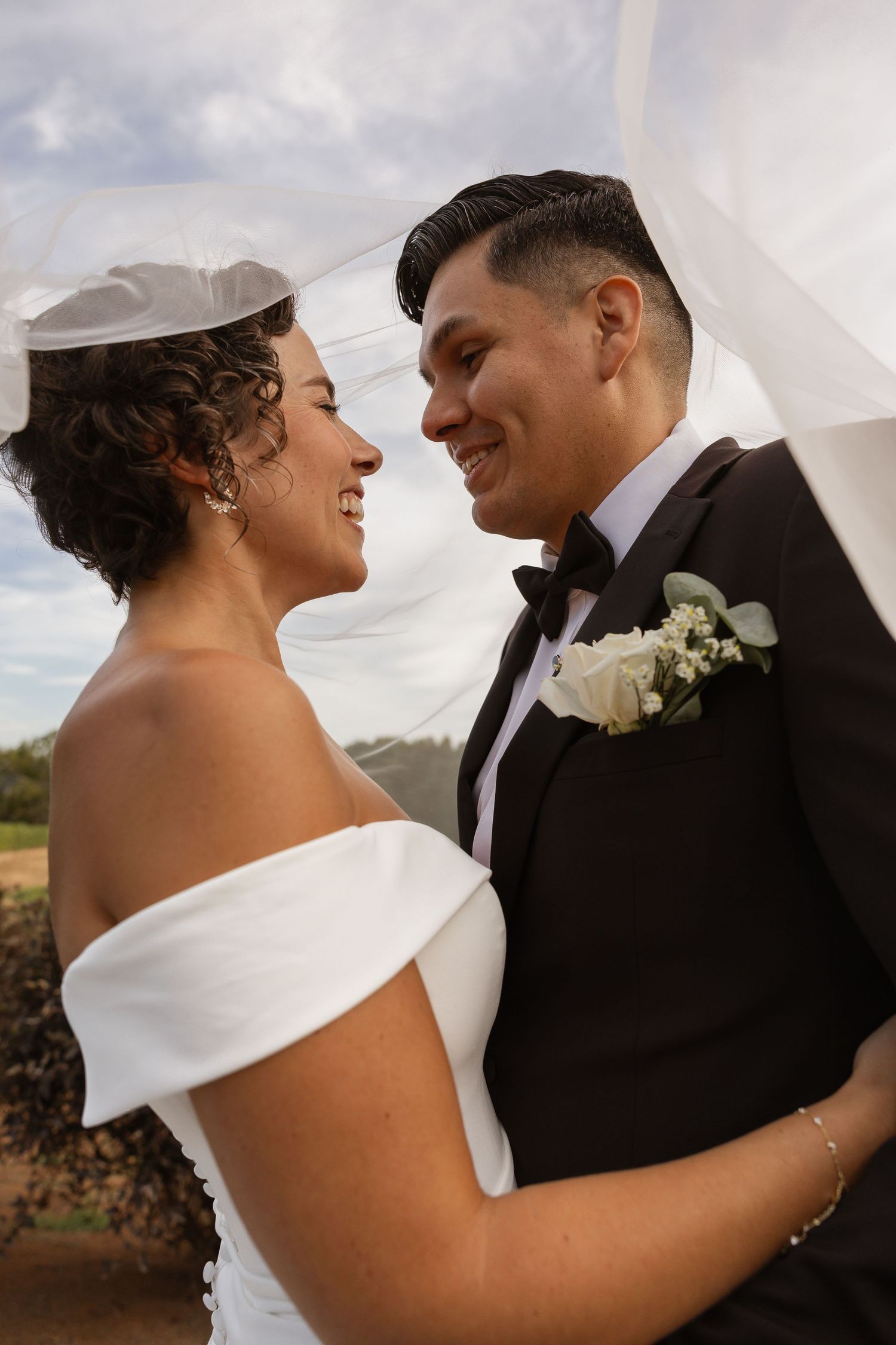 Newlyweds share a tender moment against a cloudy sky during their outdoor wedding.