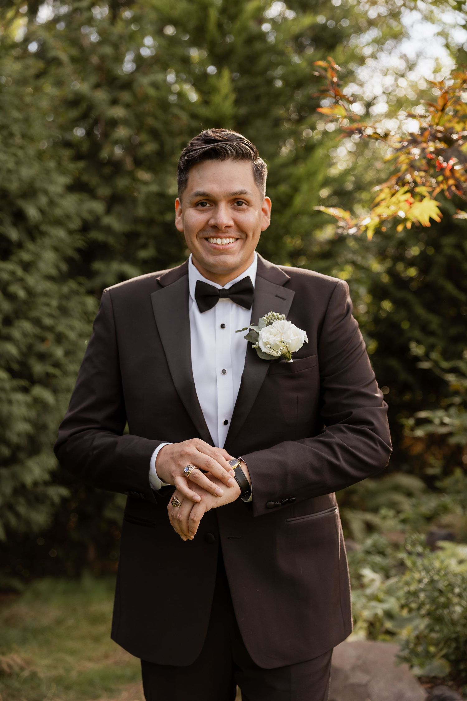 Wedding photos show someone in a classic black tuxedo with white boutonniere posing outdoors against autumn foliage.