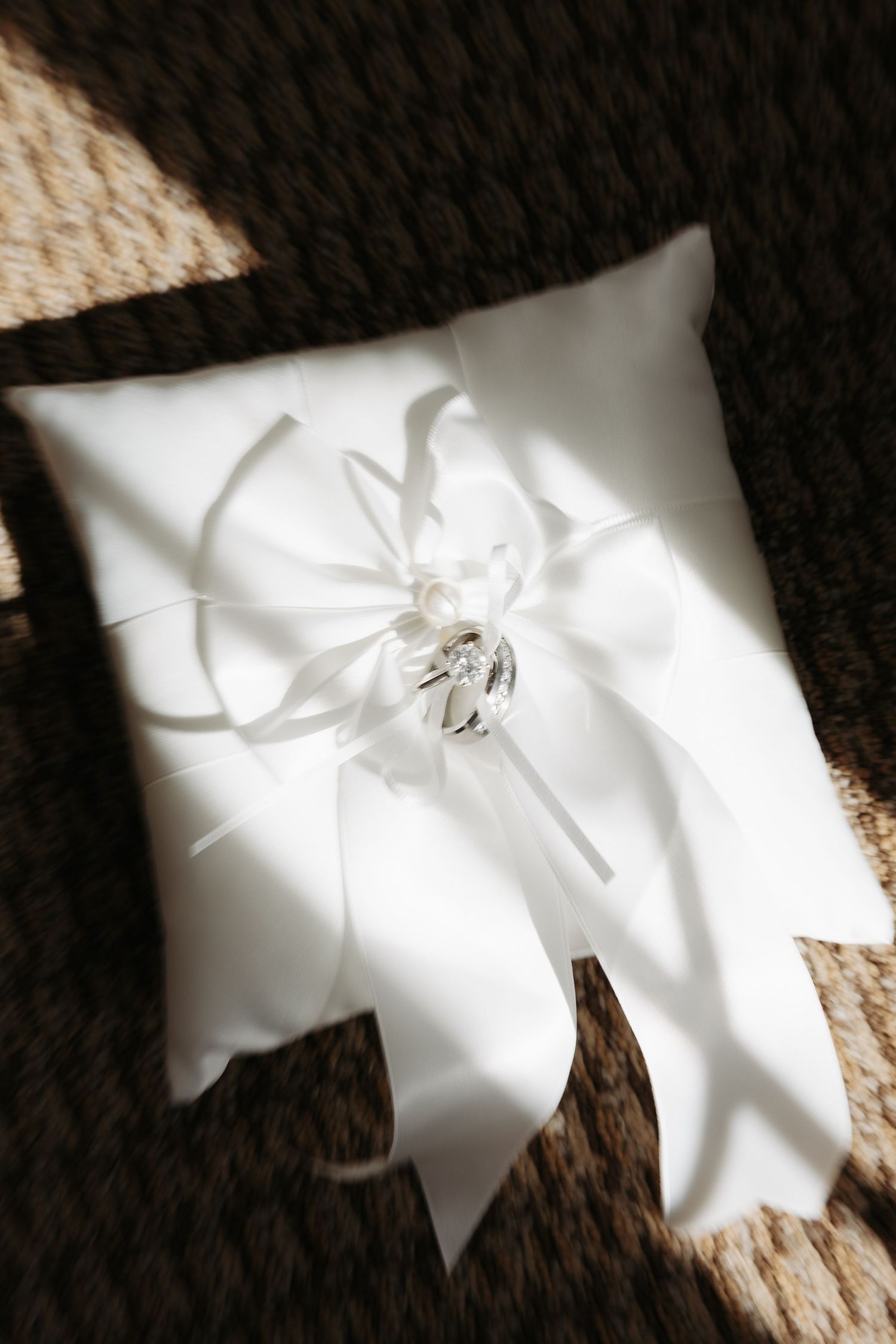 White satin ring bearer pillow with delicate bow detail casting soft shadows.