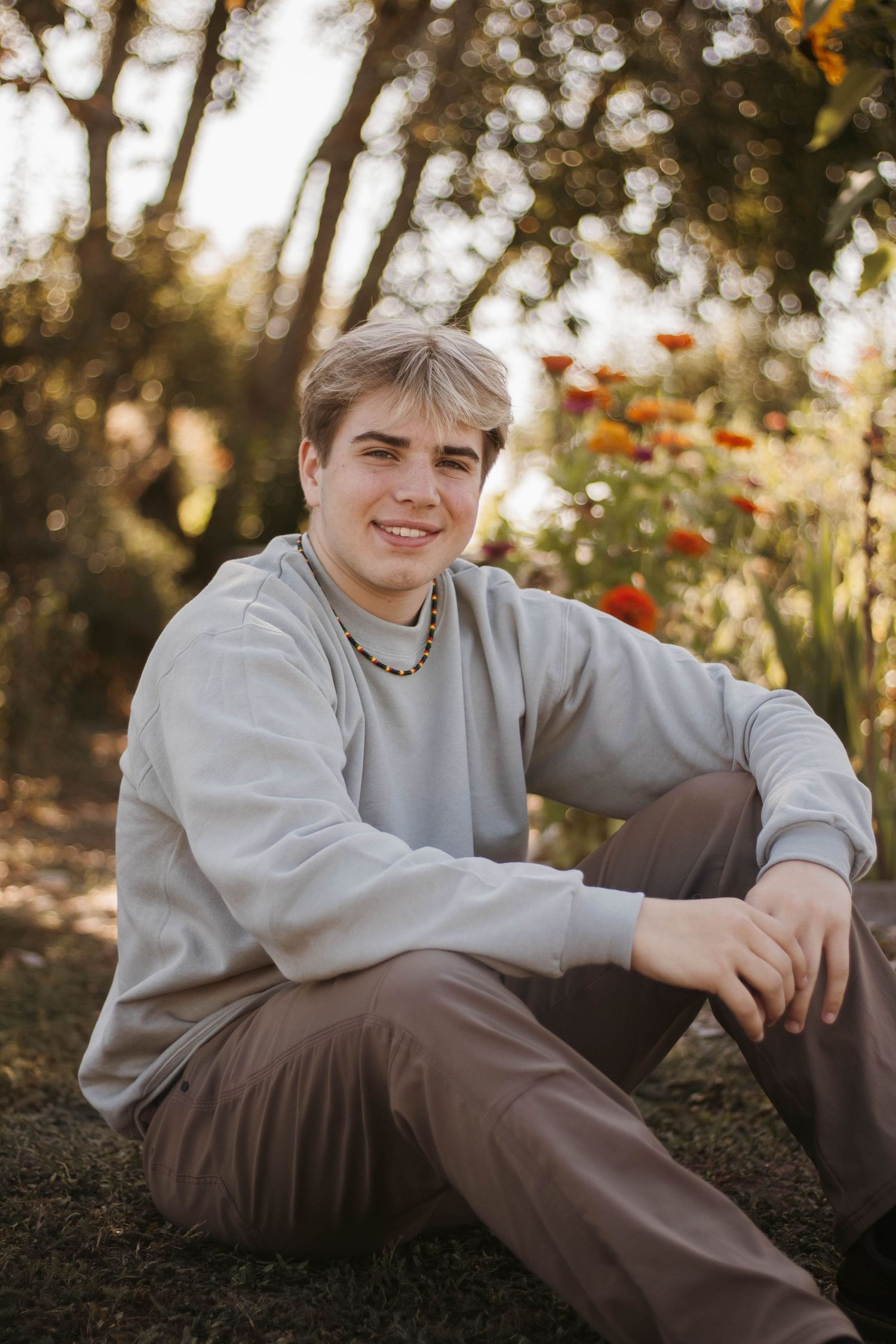 A person in a gray sweatshirt sits casually outdoors during golden hour with autumn foliage in the background.