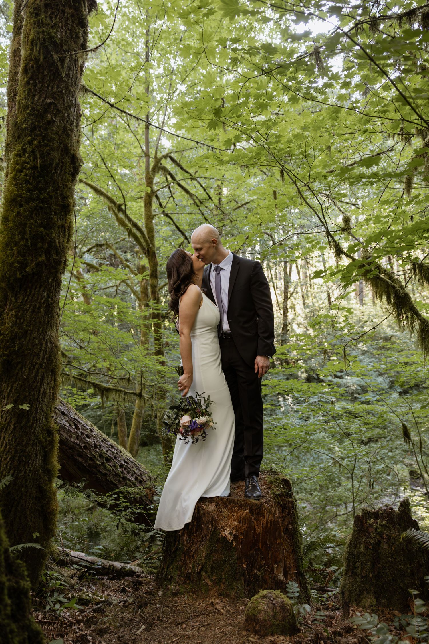 A romantic wedding moment captured in a serene forest setting with tall trees and natural lighting.