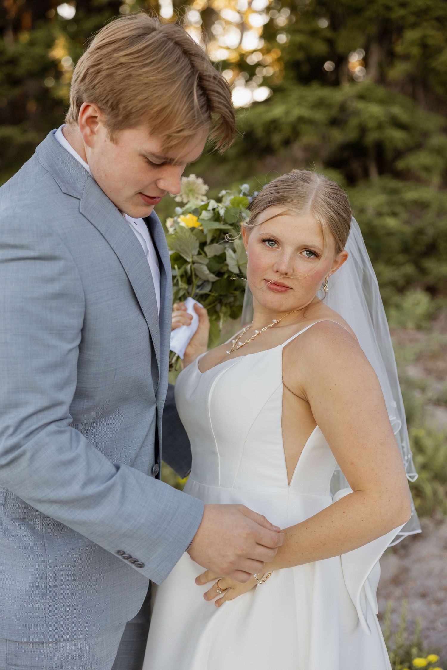 A romantic wedding couple shares intimate moments in a garden setting at sunset while wearing gray suit and white dress.
