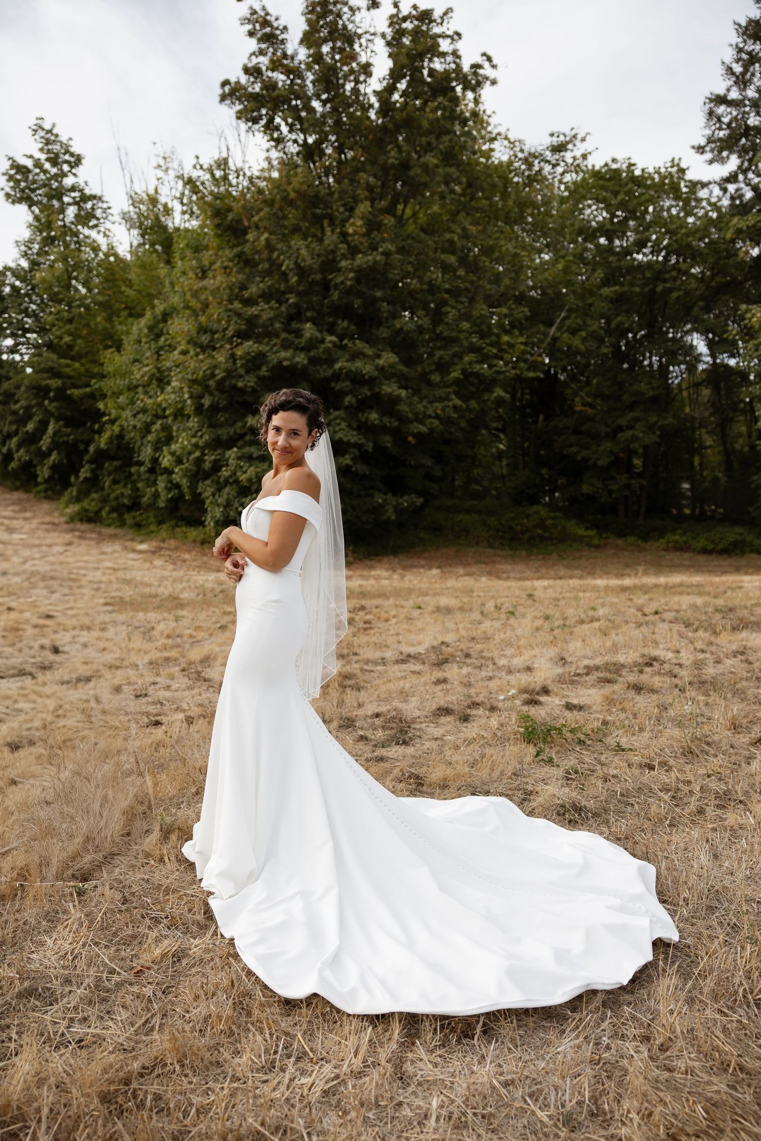 A bride in a classic white gown with dramatic train poses in a rustic outdoor setting.