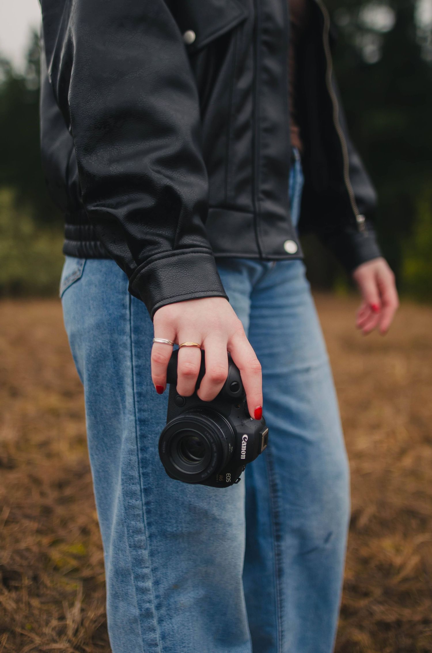 Close-up view of someone holding a black camera against blue jeans in an outdoor setting.