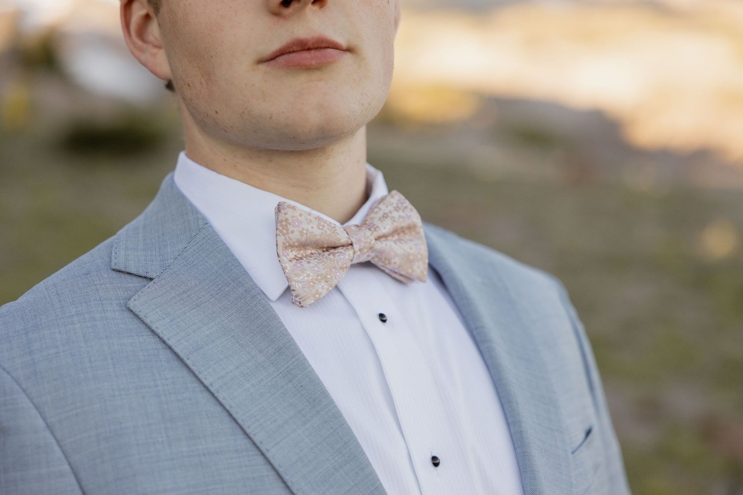 Formal attire details showing light gray suit jacket and peach bow tie.