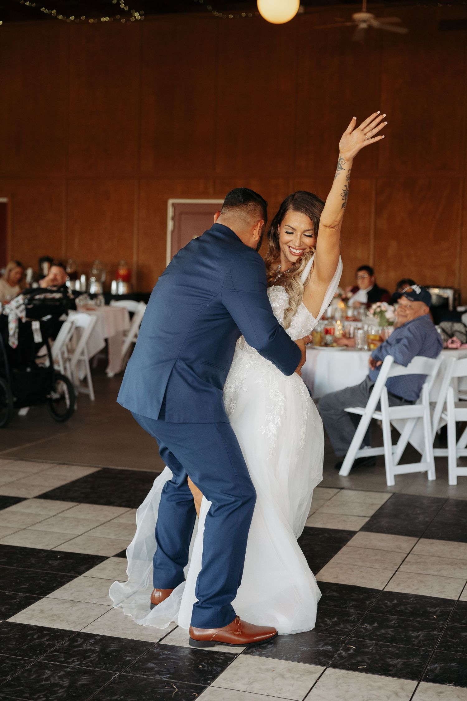 Wedding couple performing a playful dance dip on a black and white checkered floor.