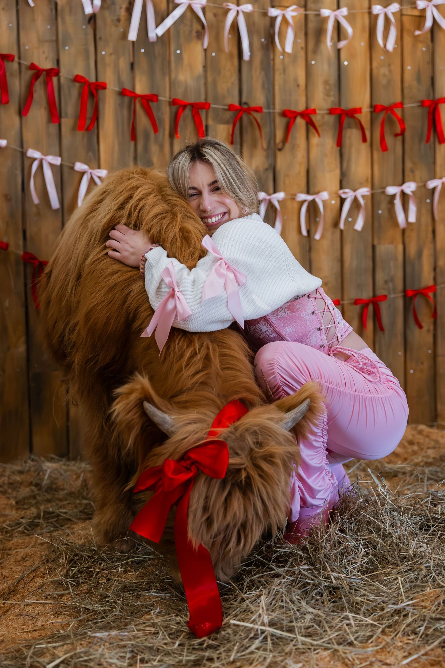 A large brown rooster interacts with a pink-dressed figure in a rustic barn setting with decorative bunting overhead.