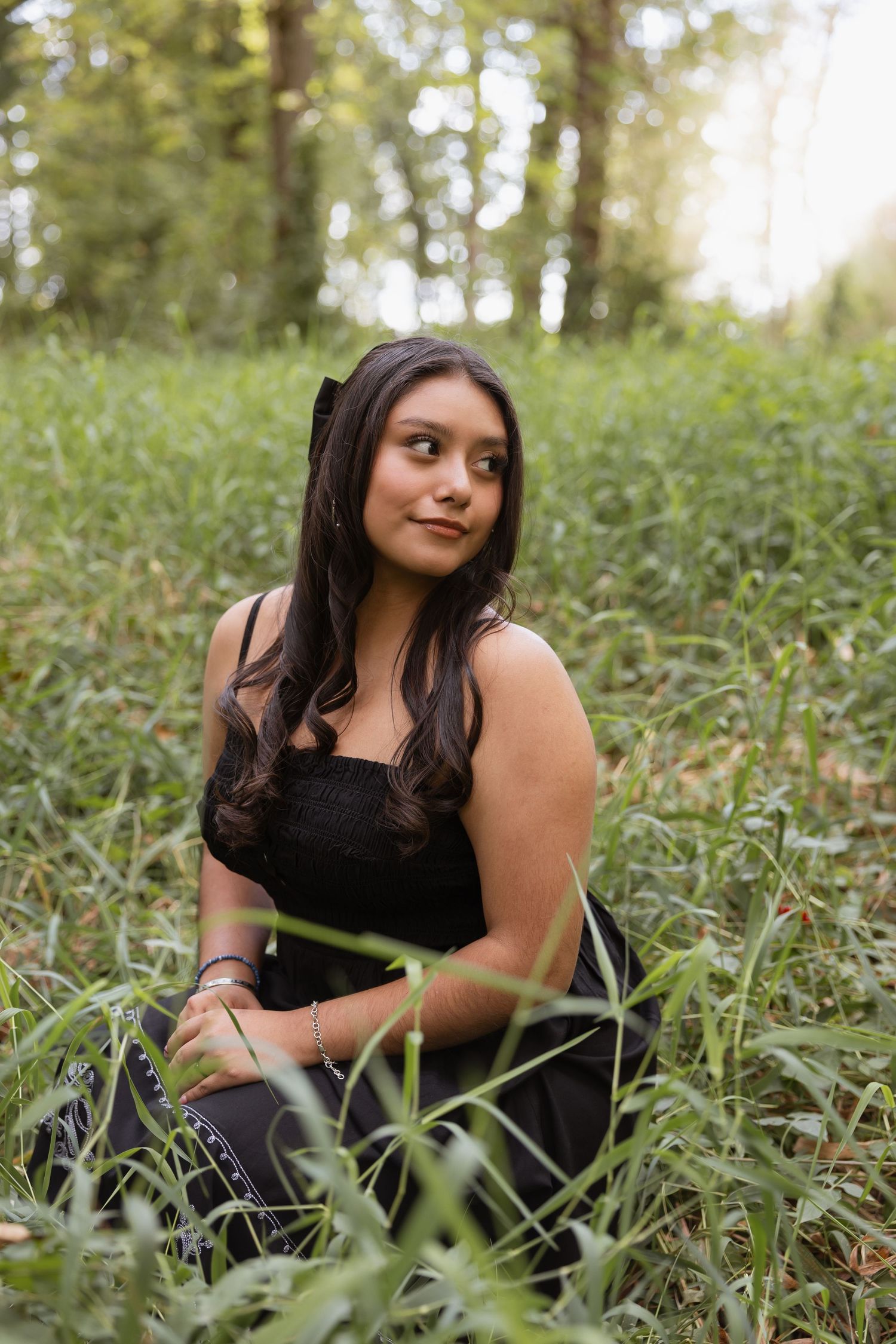 A person in a black top poses gracefully in tall grass during a golden hour outdoor photoshoot.