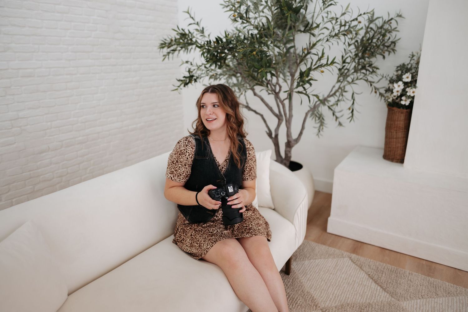 Studio photography session with person holding camera against white brick wall and indoor plant.