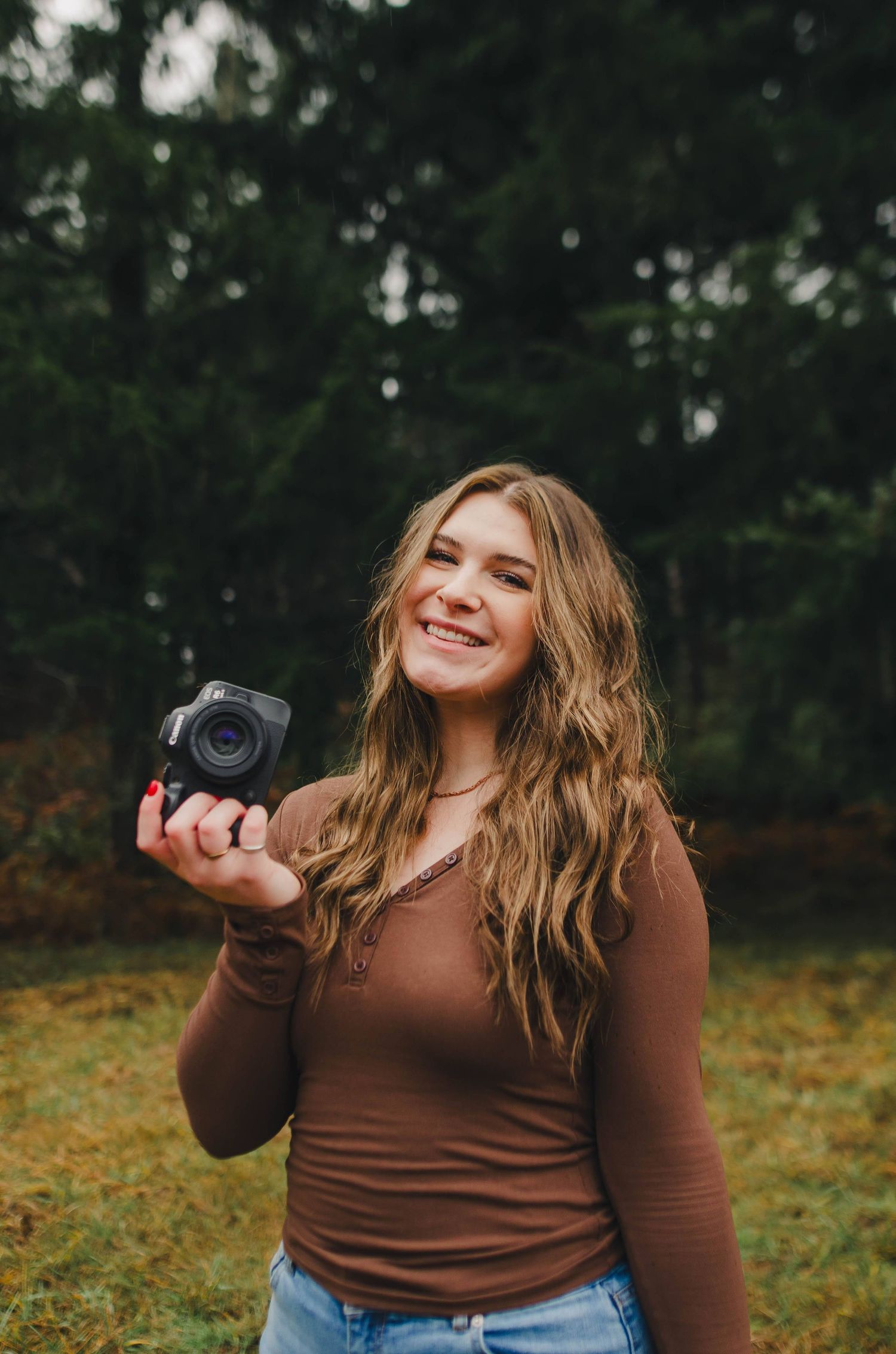 Woman photographer in brown top holding camera outdoors in autumn setting.