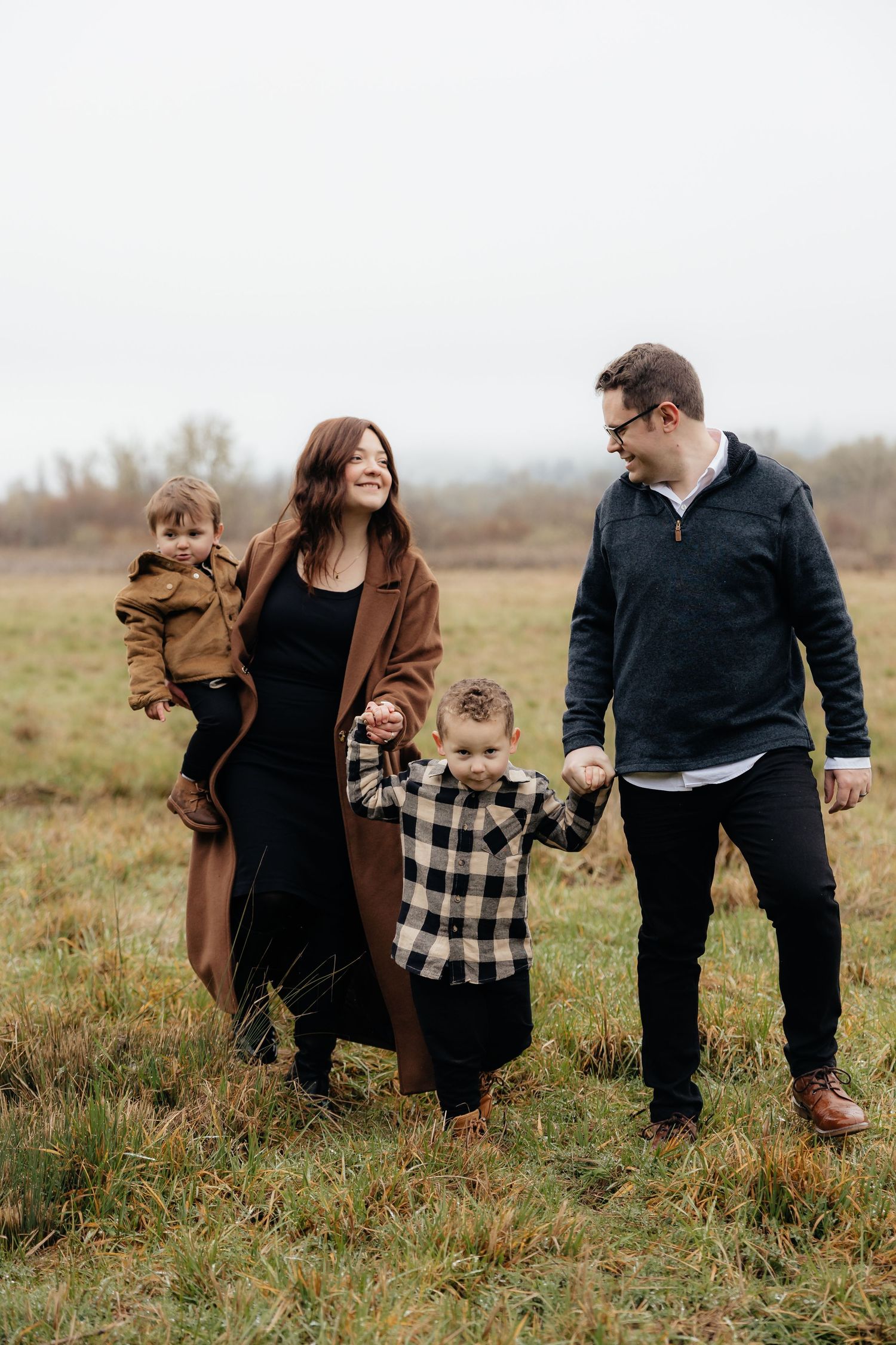 A family in brown and black outfits shares playful moments together in a grassy autumn field.