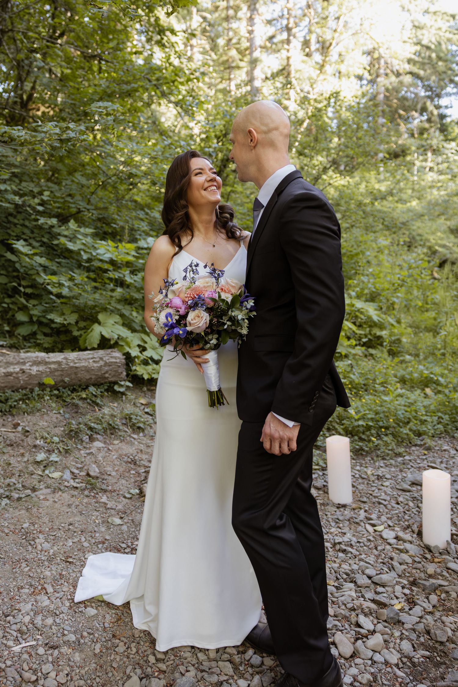A couple shares joyful moments during their outdoor forest wedding ceremony surrounded by candles and natural greenery.