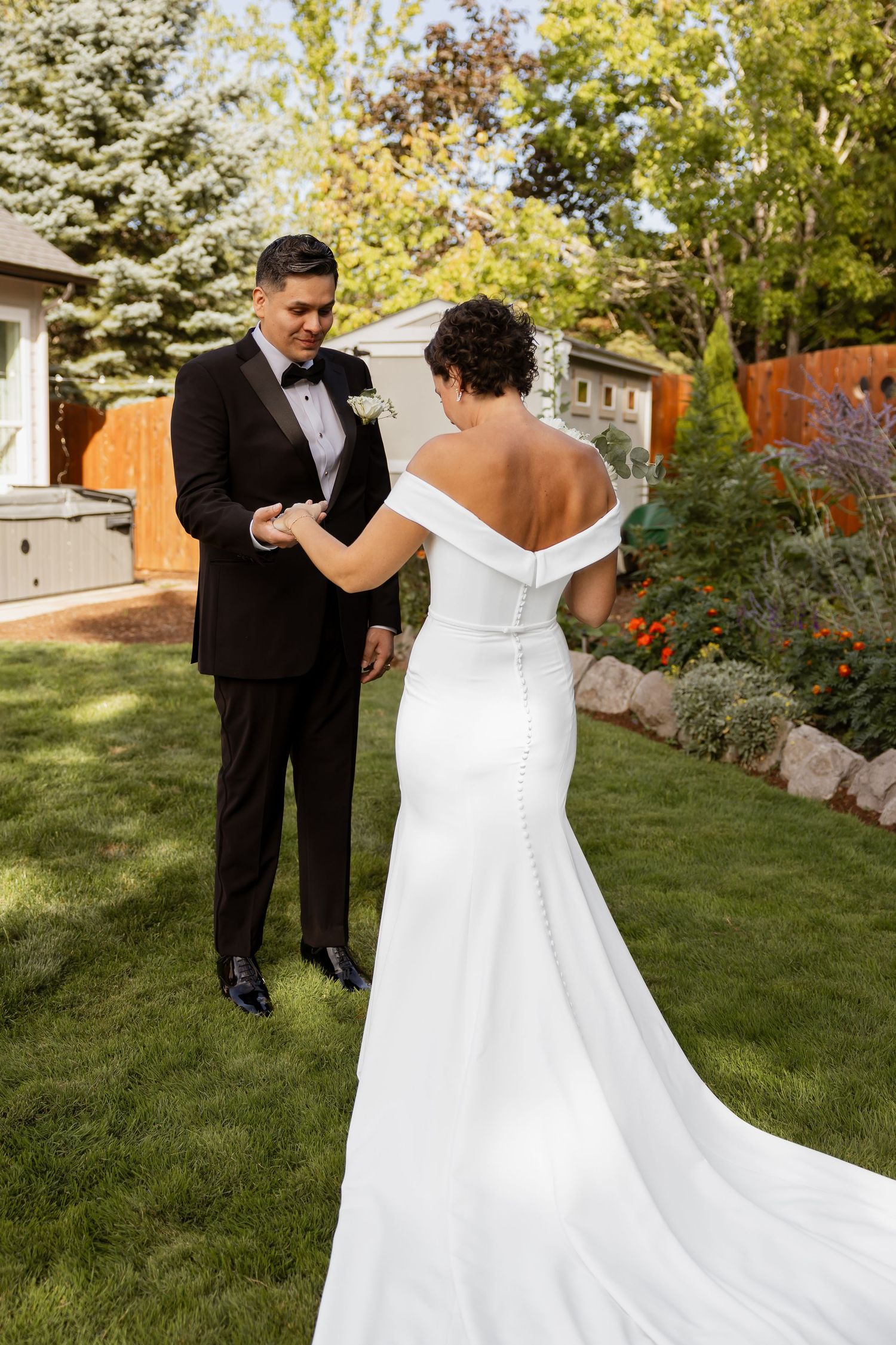 Bride in off-shoulder gown dances with groom on lush green lawn during outdoor wedding celebration.