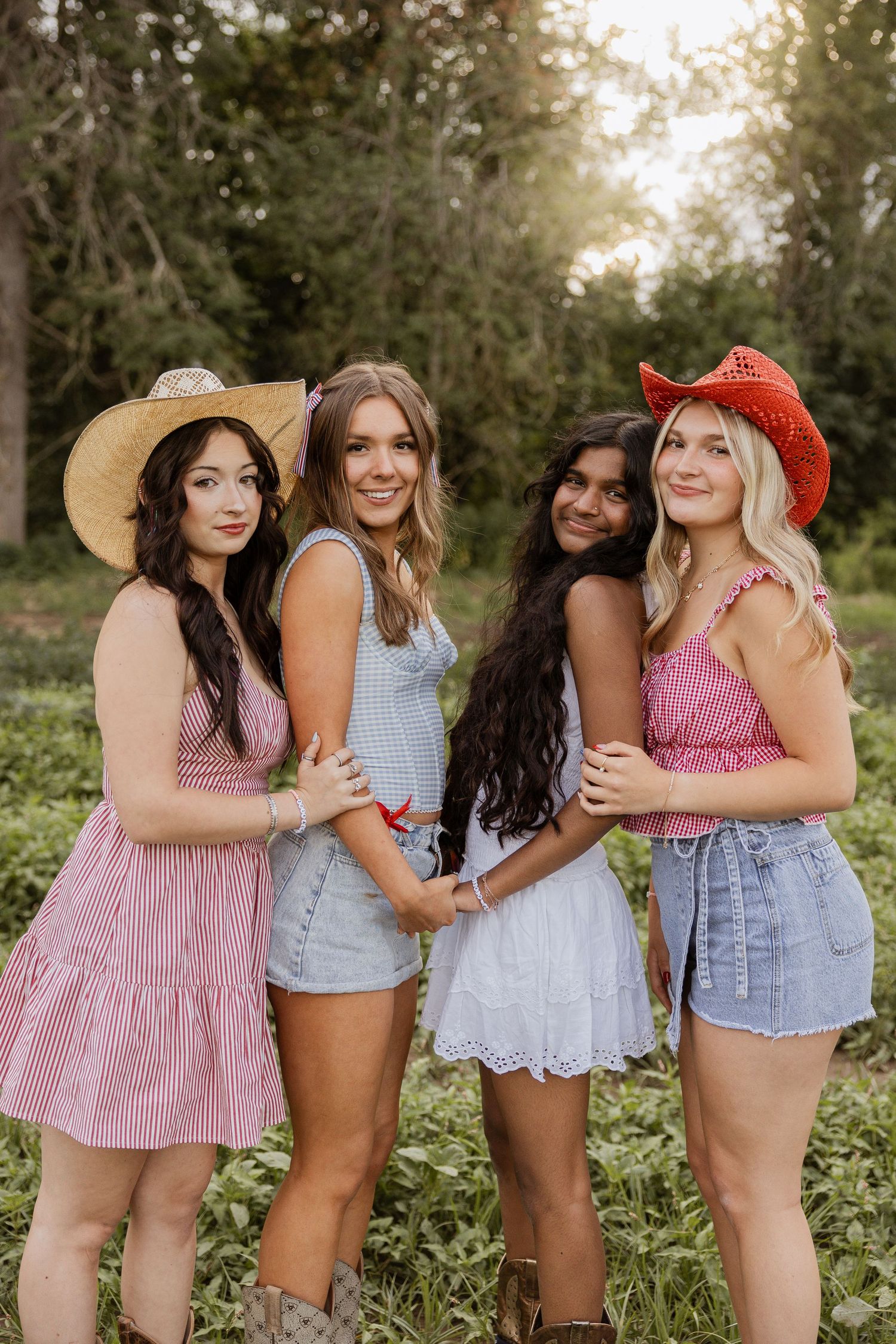 A group of friends in summer outfits and cowboy hats pose together outdoors in a sunlit field.