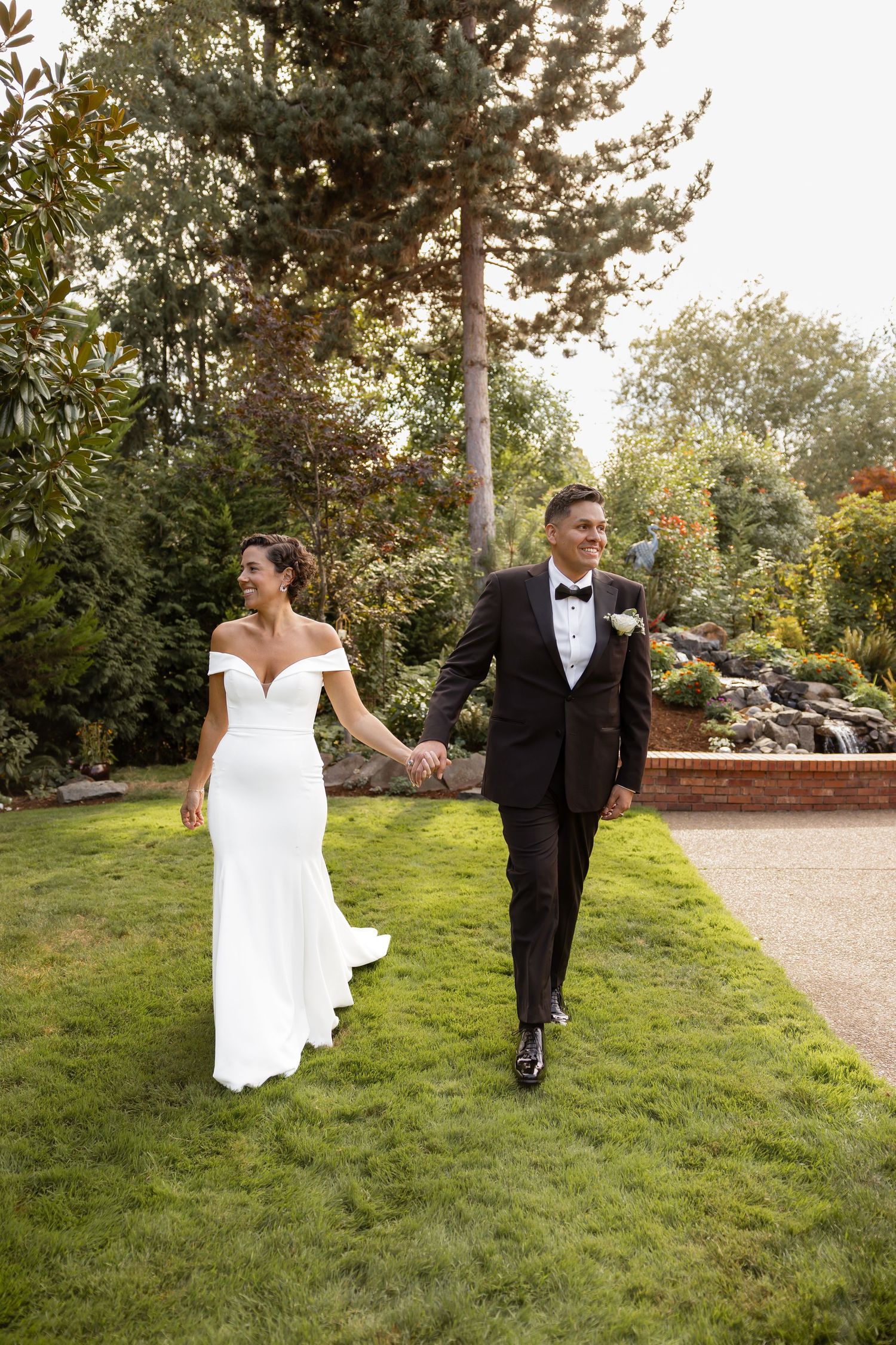 Wedding couple running playfully on green grass with trees in the background.